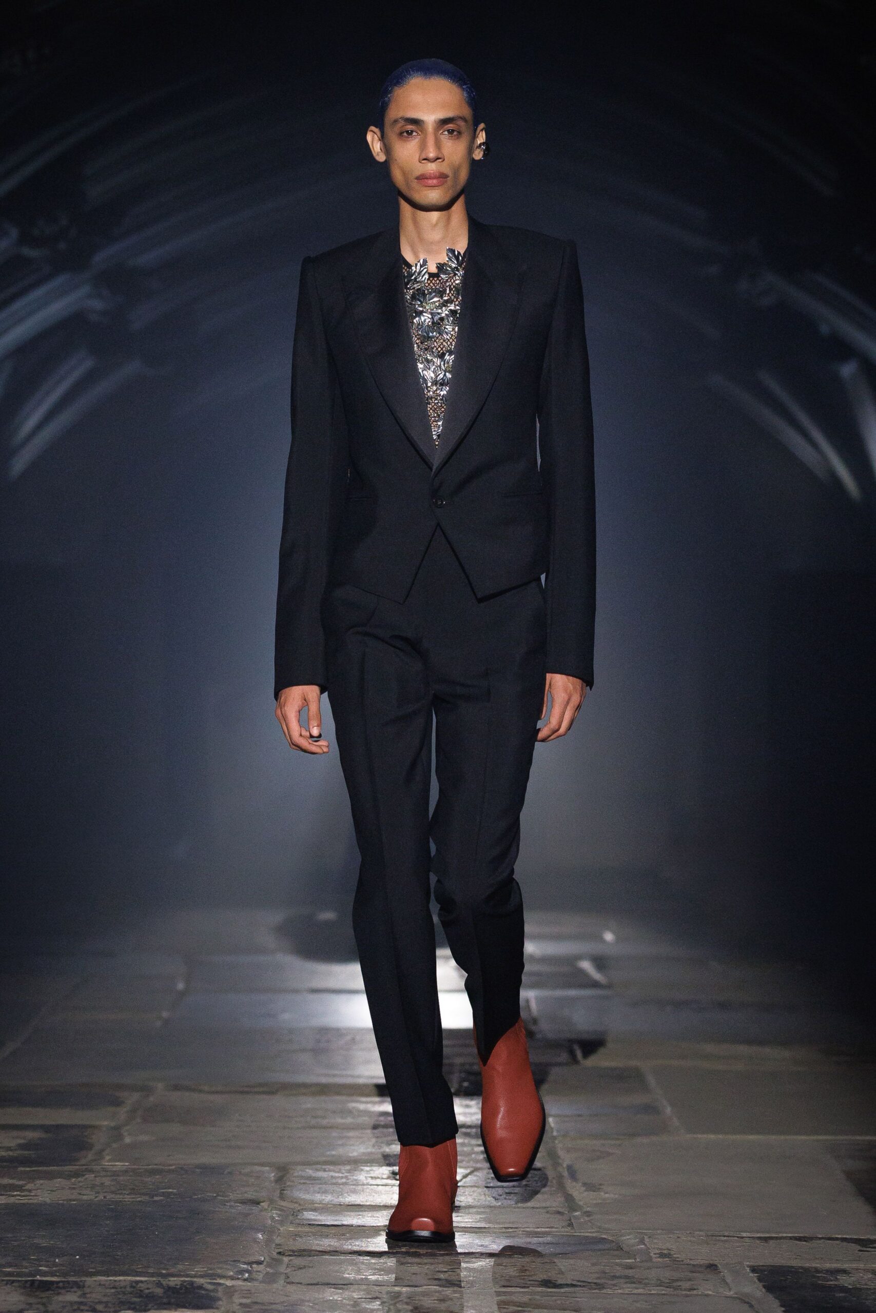 Black tailored blazer with peaked lapels and a single low button. Silver-black sequined top, neckline cut into jagged leaflike points. Slim black trousers with a sharp crease breaking over the ankle. Rust leather ankle boots with blunt squared toes. Crossing a stone cloister just after the bells stopped.