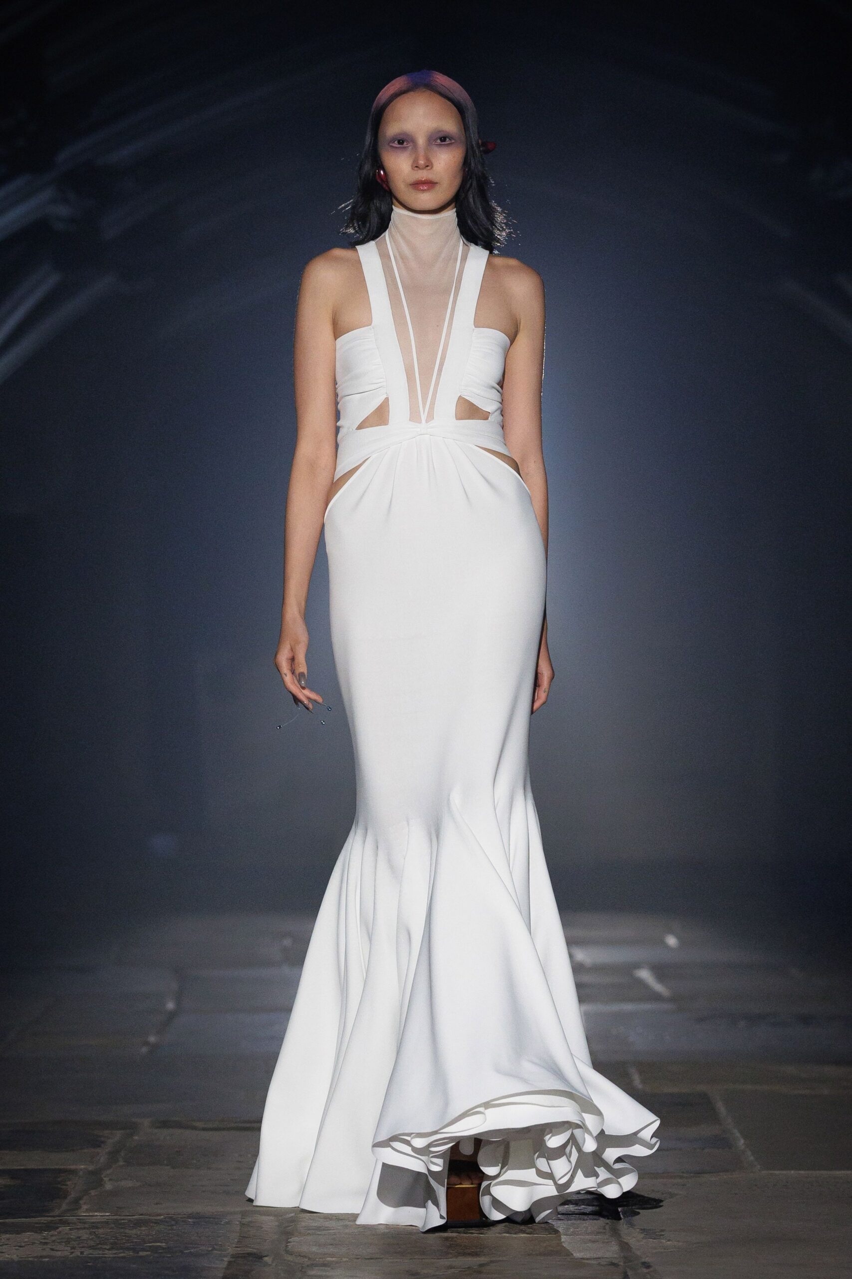 White crepe column gown with sheer mesh turtleneck and plunging strap insets. Brown platform soles barely showing beneath the rippling fishtail hem. Civil wedding at noon, then straight onto old church flagstones.
