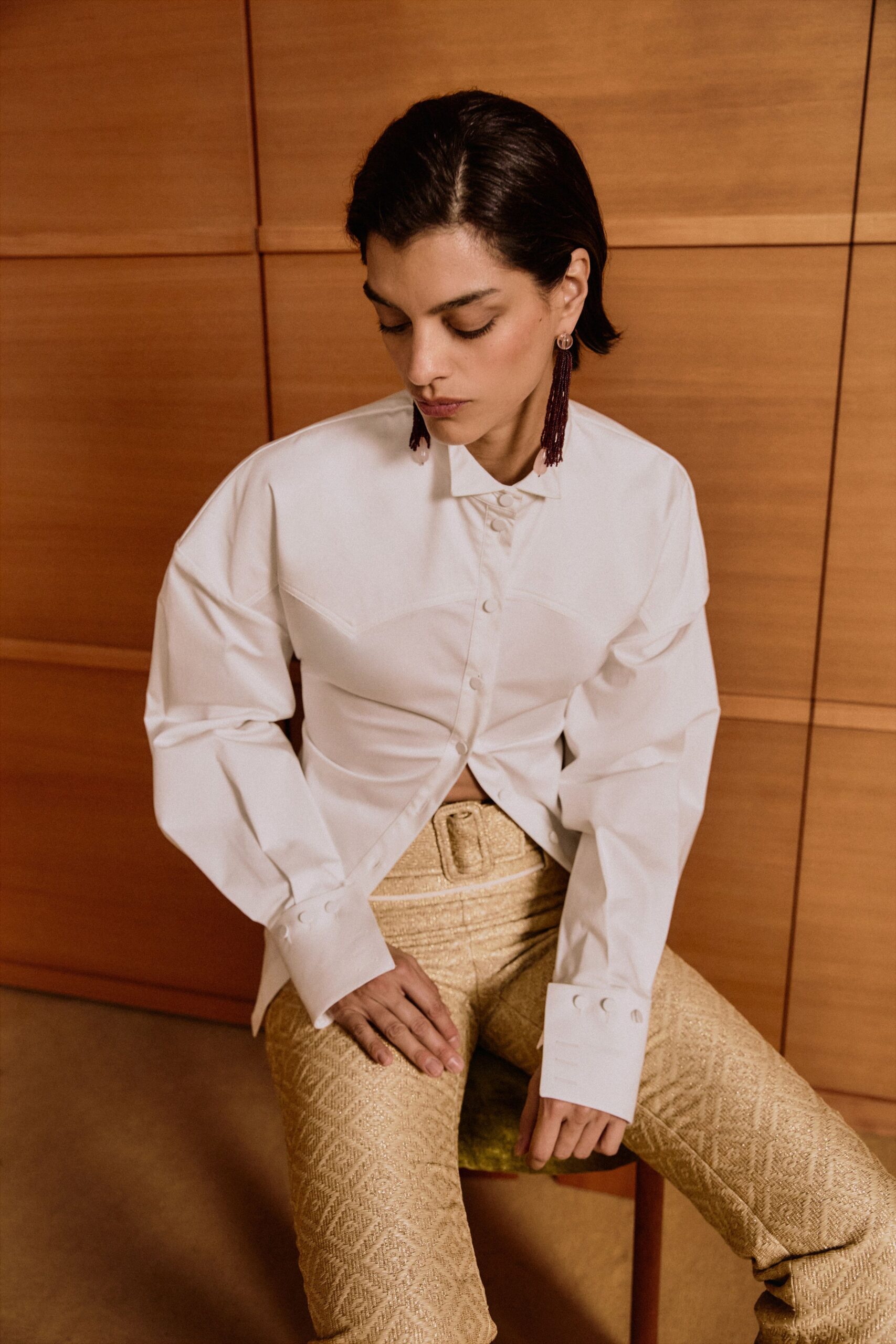 Long oxblood bead tassels tipped with pale pink drops. Crisp white cotton shirt, curved yoke seams and extra-long button cuffs. Gold jacquard trousers with a diamond weave and covered buckle belt. For a hotel bar wedding where someone keeps opening the terrace doors.
