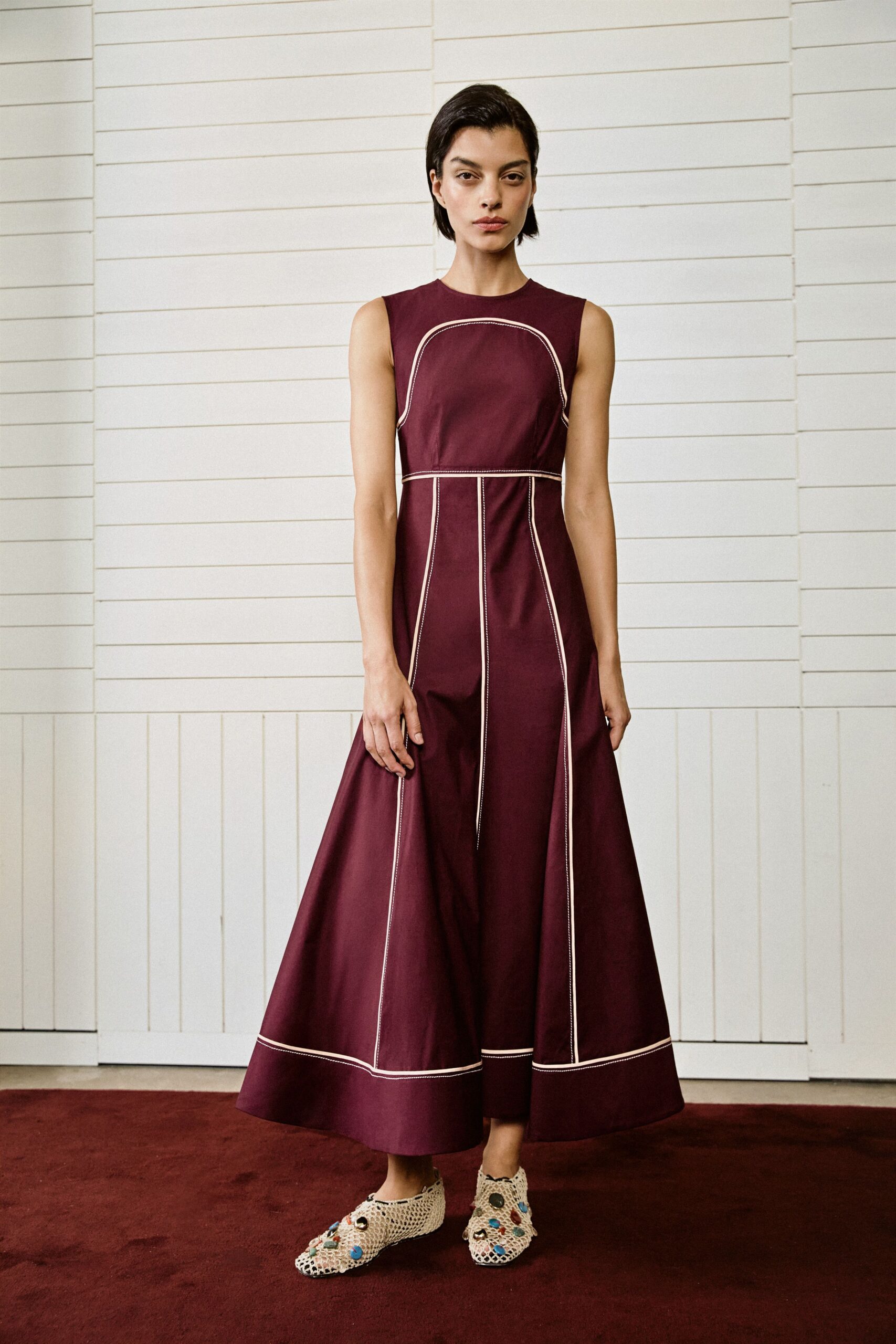 Burgundy sleeveless dress in crisp twill, outlined with pale topstitched piping. Cream crocheted flats dotted with glossy cabochons across the vamp. For a courthouse wedding in a town with wraparound porches.