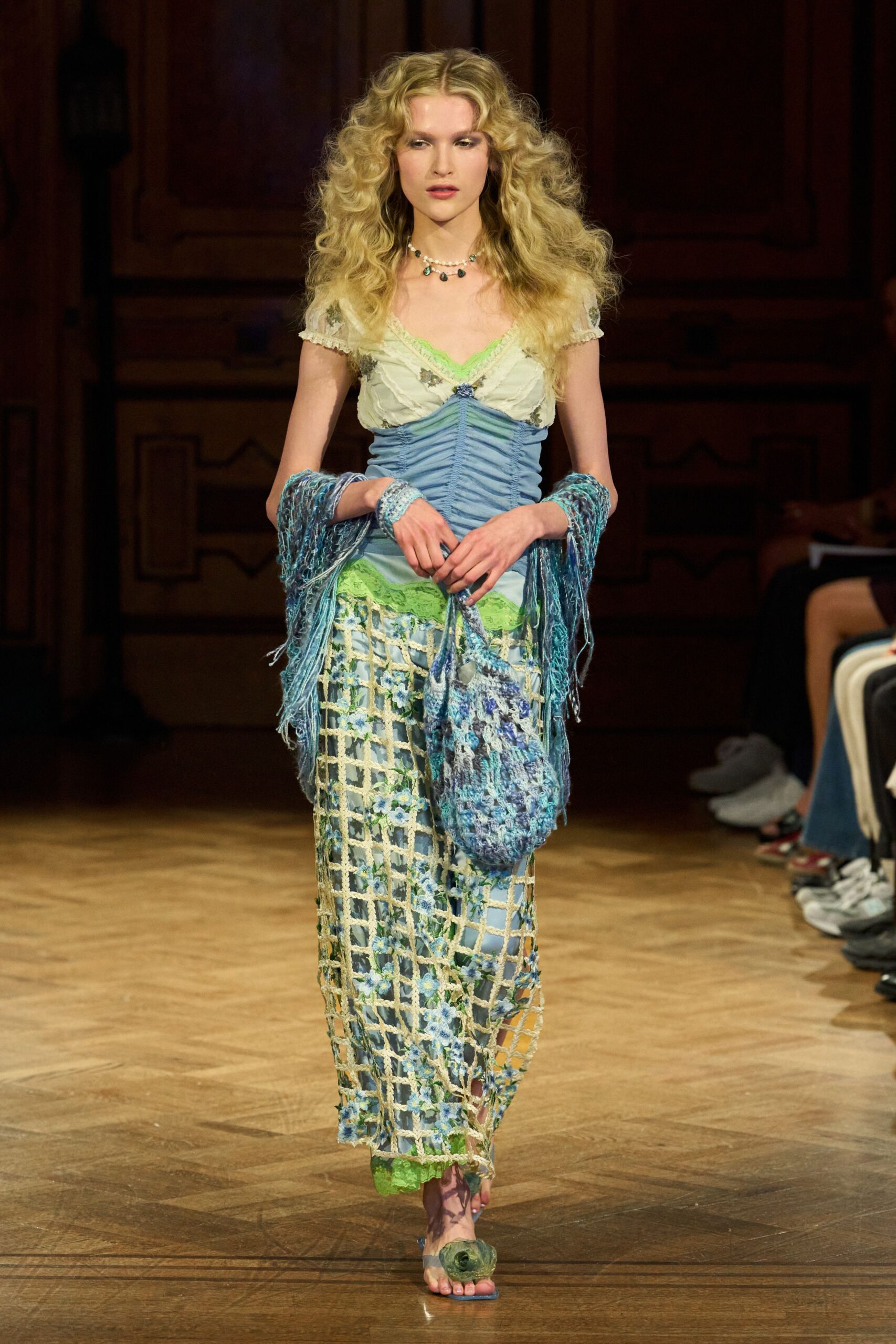 Powder-blue ruched bodice with cream floral cups and acid-lime lace. Long blue floral slip under a cream crocheted lattice. Loose blue knit shawl, fringe dragging from both wrists. Crocheted pouch in mottled blue yarn. Flat sandals with a mossy rosette over the toes. Walking back from a spa town florist with wet hair at dusk.