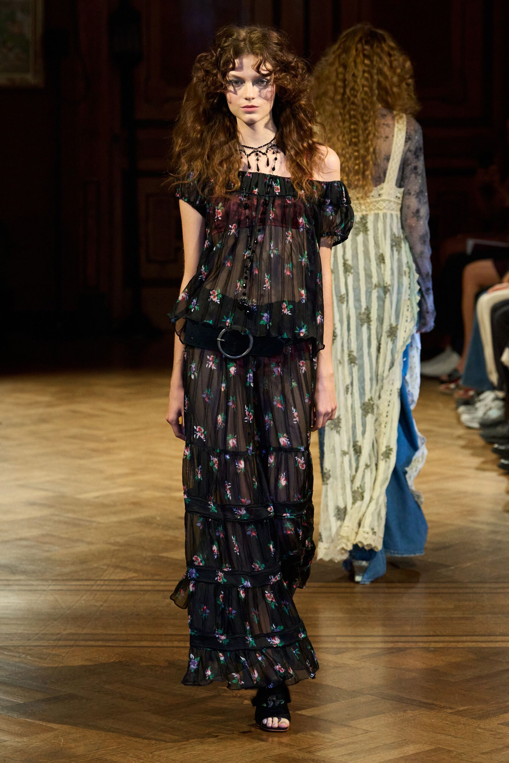 Black bead drops clustered close at the collarbone. Sheer black georgette dress scattered with tiny rose sprigs. Wide black belt with a dull silver ring buckle. Black velvet mules with a rosette over the toes. Walking the creaking corridor to breakfast in a country house gone slightly damp.