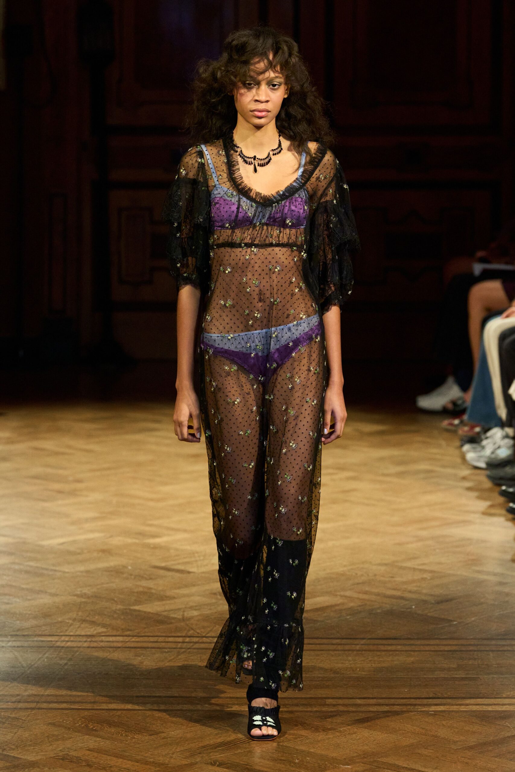 Black beaded necklace with a single teardrop pendant. Black dotted mesh dress scattered with tiny metallic florals. Violet satin bralette with pale blue straps. Matching violet briefs banded in pale blue. Black peep-toe mules with white flower beading. Crossing a creaking ballroom floor after midnight rain.