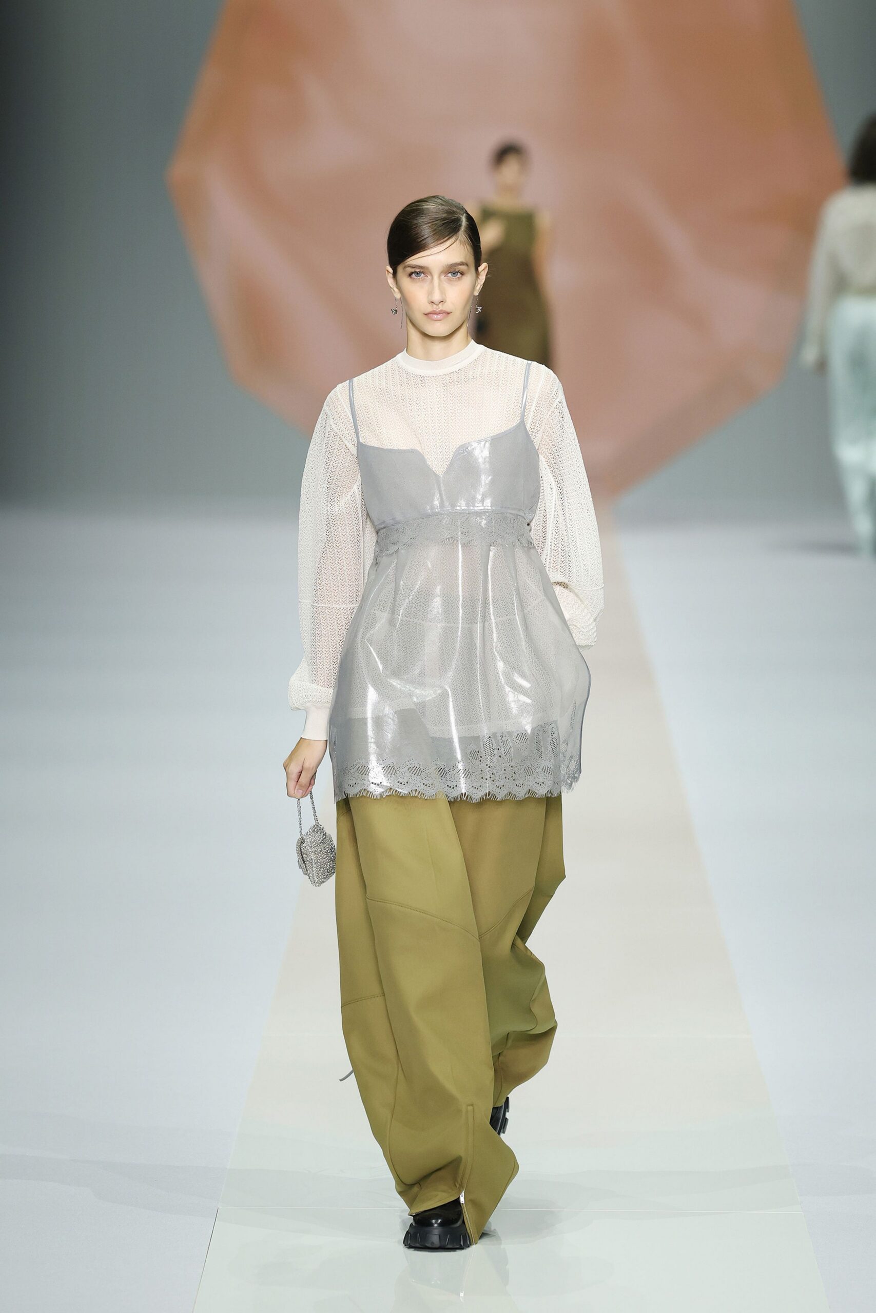 Sheer chalk open-knit top with ribbed collar and puffed cuffs. Pearly pvc slip layered over it, scalloped lace peeking below the hem. Moss wide-leg trousers with curved seam panels and a dragging break. Tiny silver beaded pouch. Black square-toe platforms. Walking across a conservatory floor just after the plants were watered.