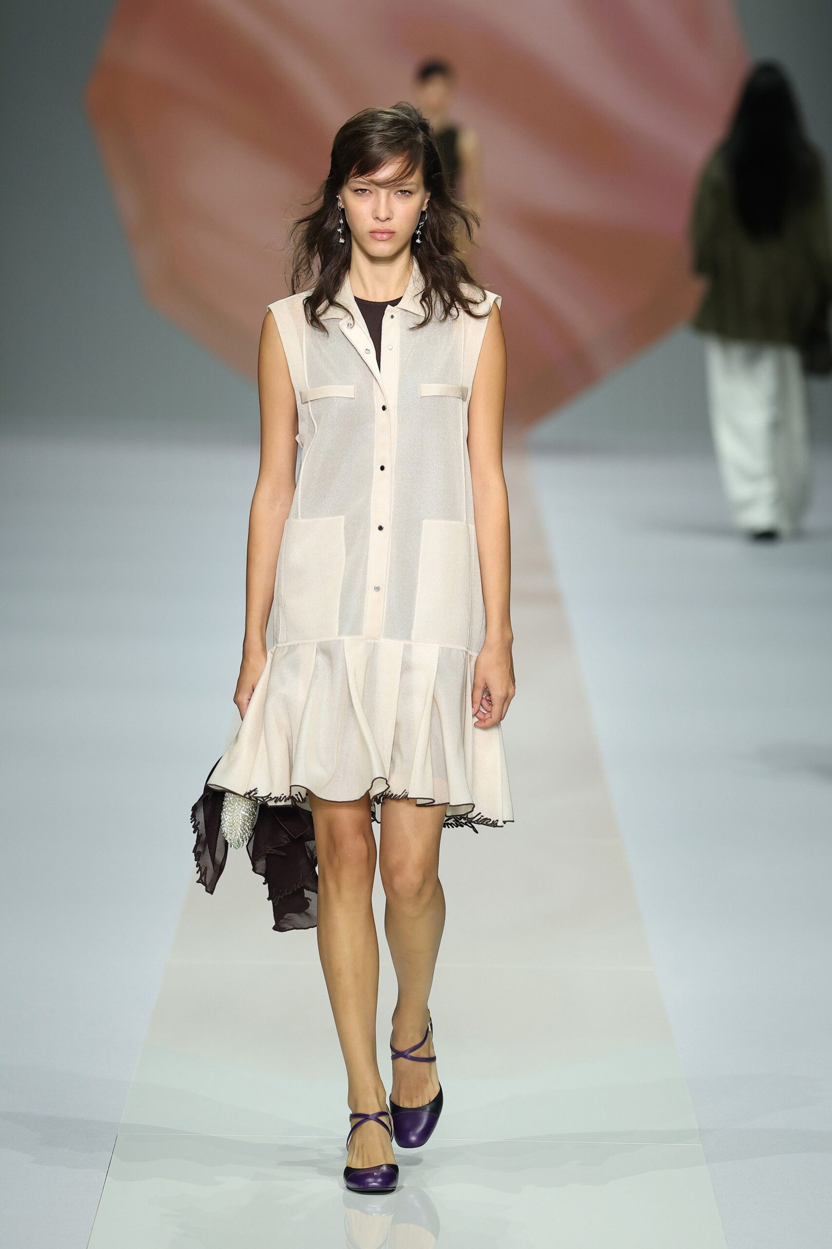 Mismatched crystal drop earrings brushing the jaw. Sleeveless chalk shirt dress in sheer crepe, black button placket and flutter hem. Black chiffon pouch with a beaded tassel spilling from one side. Purple cap-toe heels with thin crossed straps at the instep. Walking back from a hotel wedding after the grass soaked through.