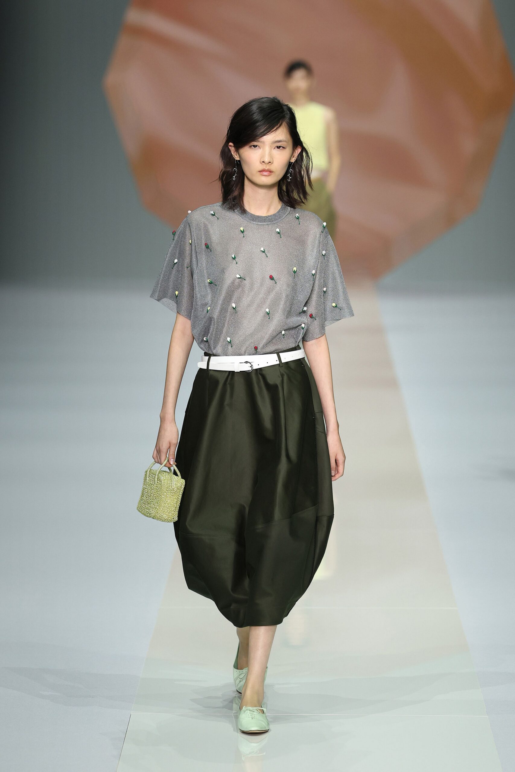 Silvery grey knit top scattered with tiny bud-like embroidery. White belt with a small off-center ring buckle. Black satin cocoon skirt, paneled into a rounded lantern shape. Pale green beaded bucket bag. Mint lace-up flats with a squared vamp. Walking back from the florist with one wrist still smelling of stems.