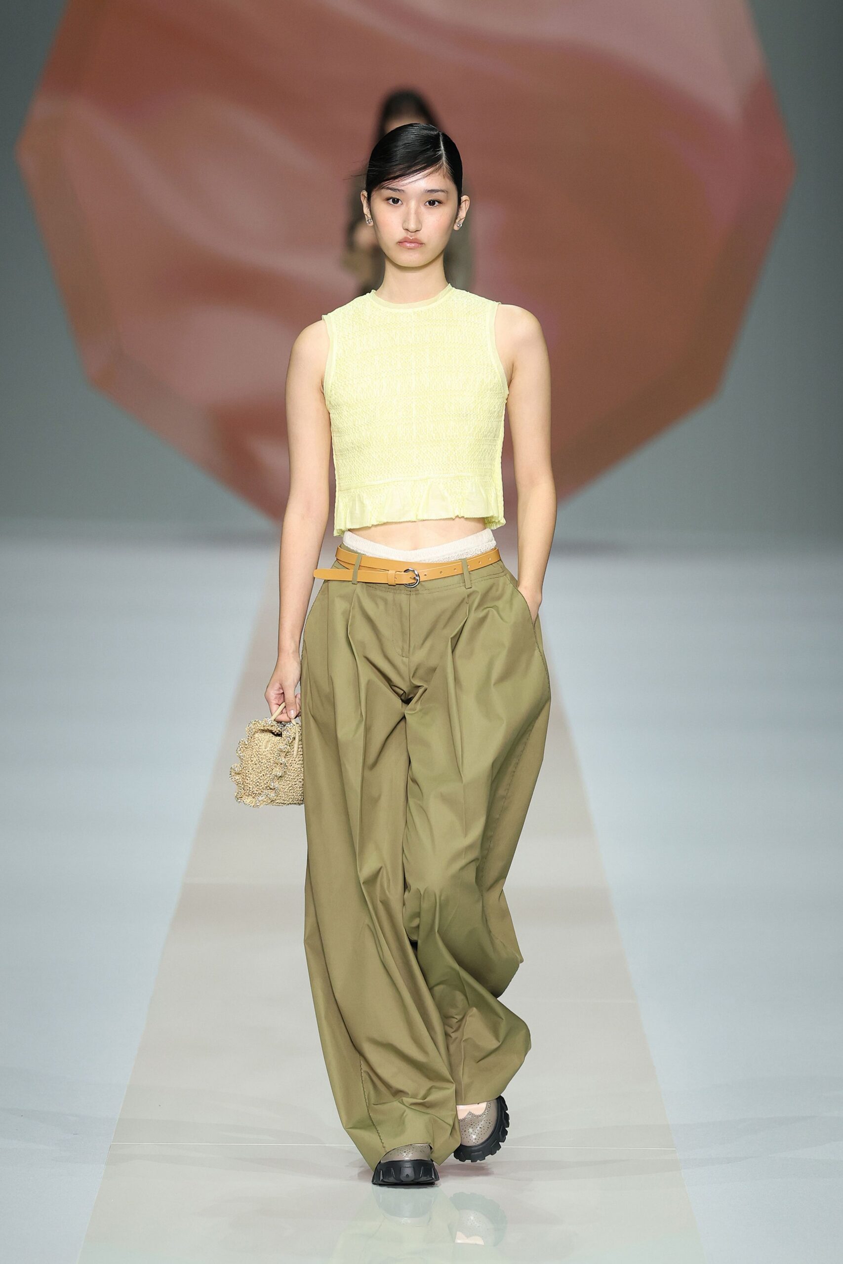 Pale butter ribbed tank with a raw little peplum hem. Olive cotton trousers cut extra wide, pleats swelling from the waistband. Tan leather belt doubled through a small silver ring. Nubby crocheted hand bag. Taupe mesh slip-ons with black rubber bumpers. Walking back from the beach snack bar with sand still on your ankles.