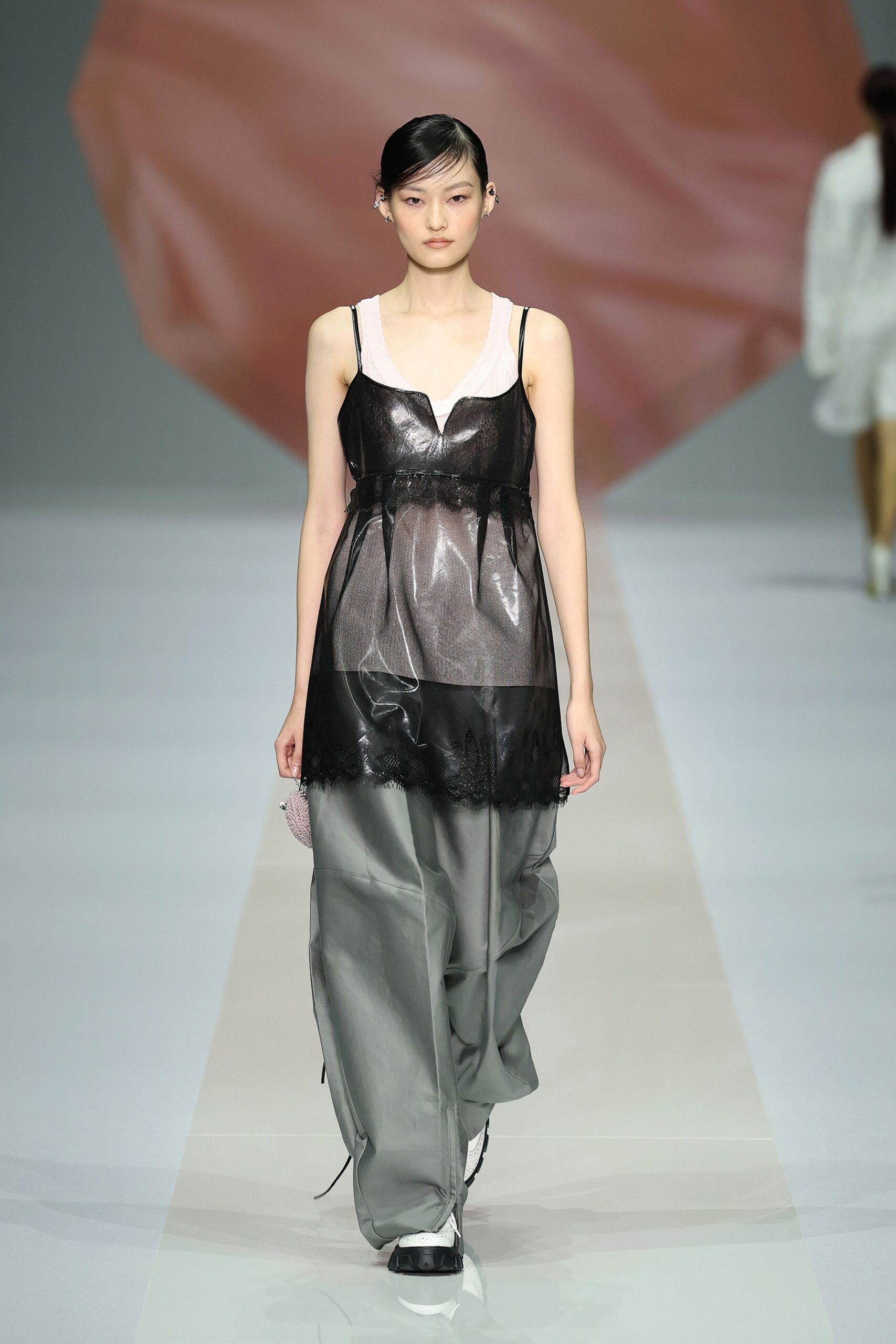 Pale blush ribbed tank with a scooped neckline peeking above. Black sheer slip with a glossy bust panel and eyelash-lace hem. Dove-grey wide trousers in papery fabric, cords dragging at the cuffs. Beaded pink wrist pouch. White sneakers with black rubber toes. For buying lilies and dish soap after sleeping somewhere else.