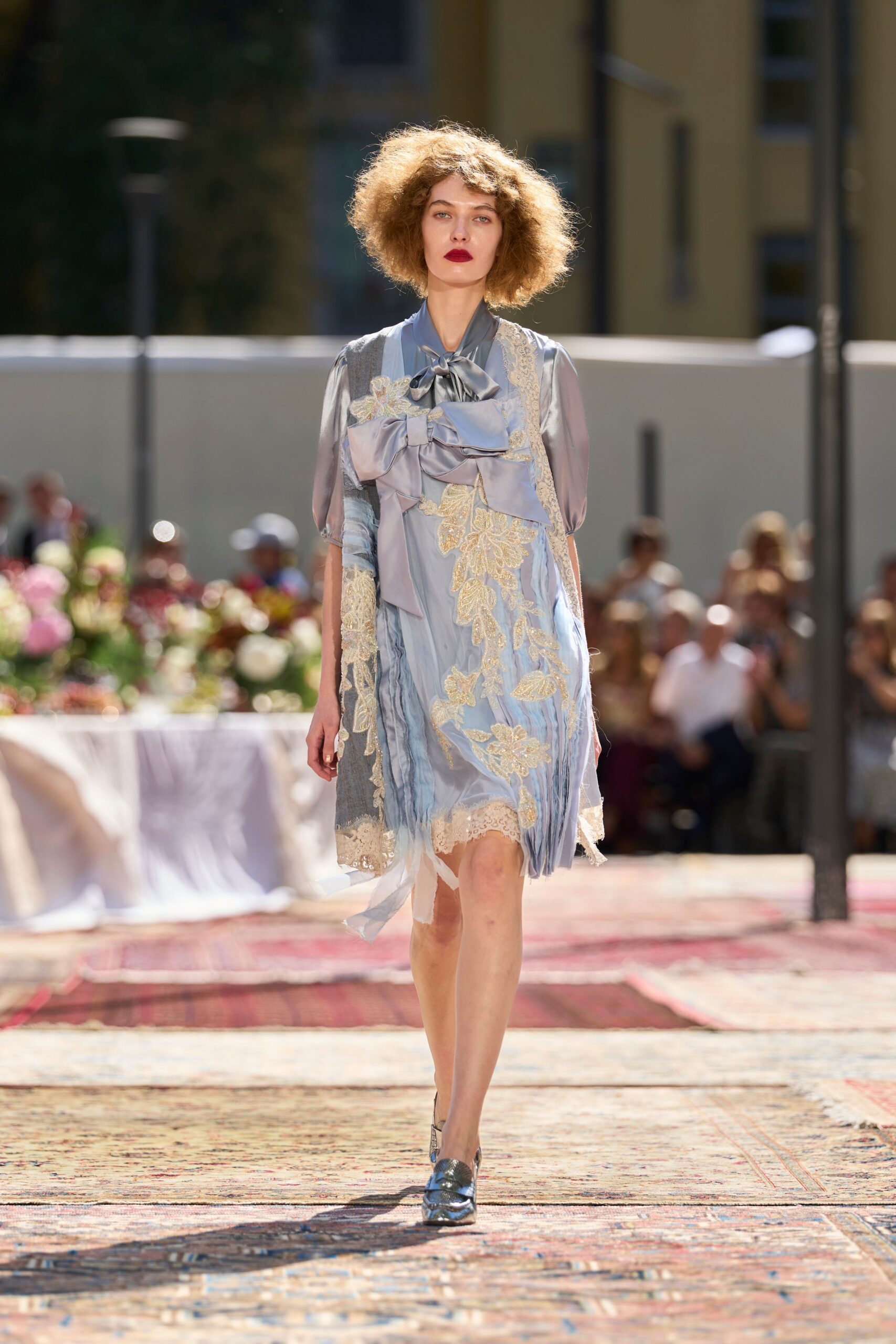 Powder-blue satin dress, paneled with cream lace and oversized bows. Sheer dove blouse underneath, tied in a limp pussy-bow at the throat. Blue-grey loafers with a bruised metallic shine. Garden luncheon after the heat has wilted the table flowers.