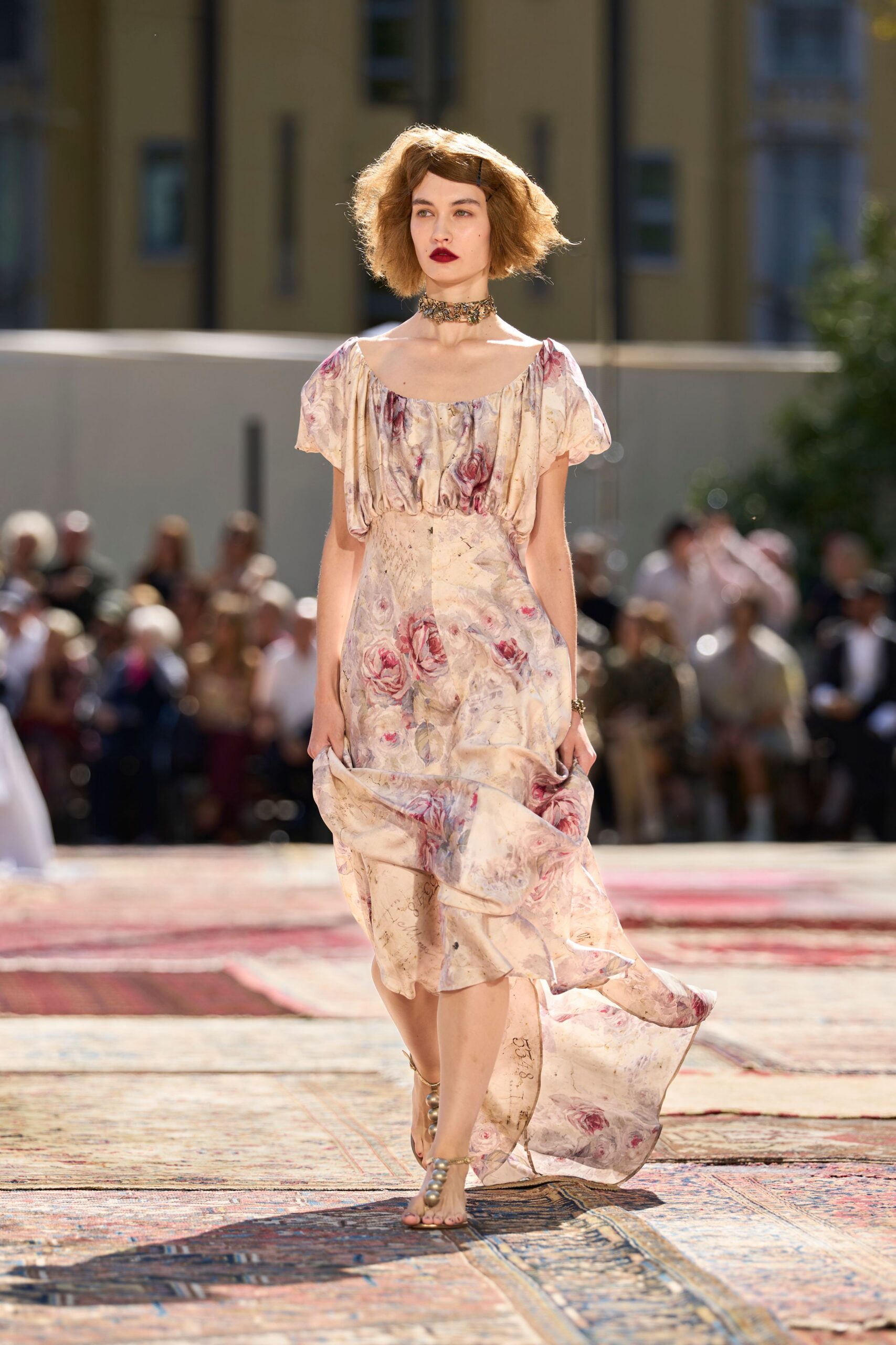 Oxidized floral choker packed close around the throat. Cream silk dress washed with faded roses, puff sleeves and a dropped handkerchief train. Barely there sandals with oversized pearl beads climbing the ankle. Walking across sun-struck rugs after a garden wedding has run late.