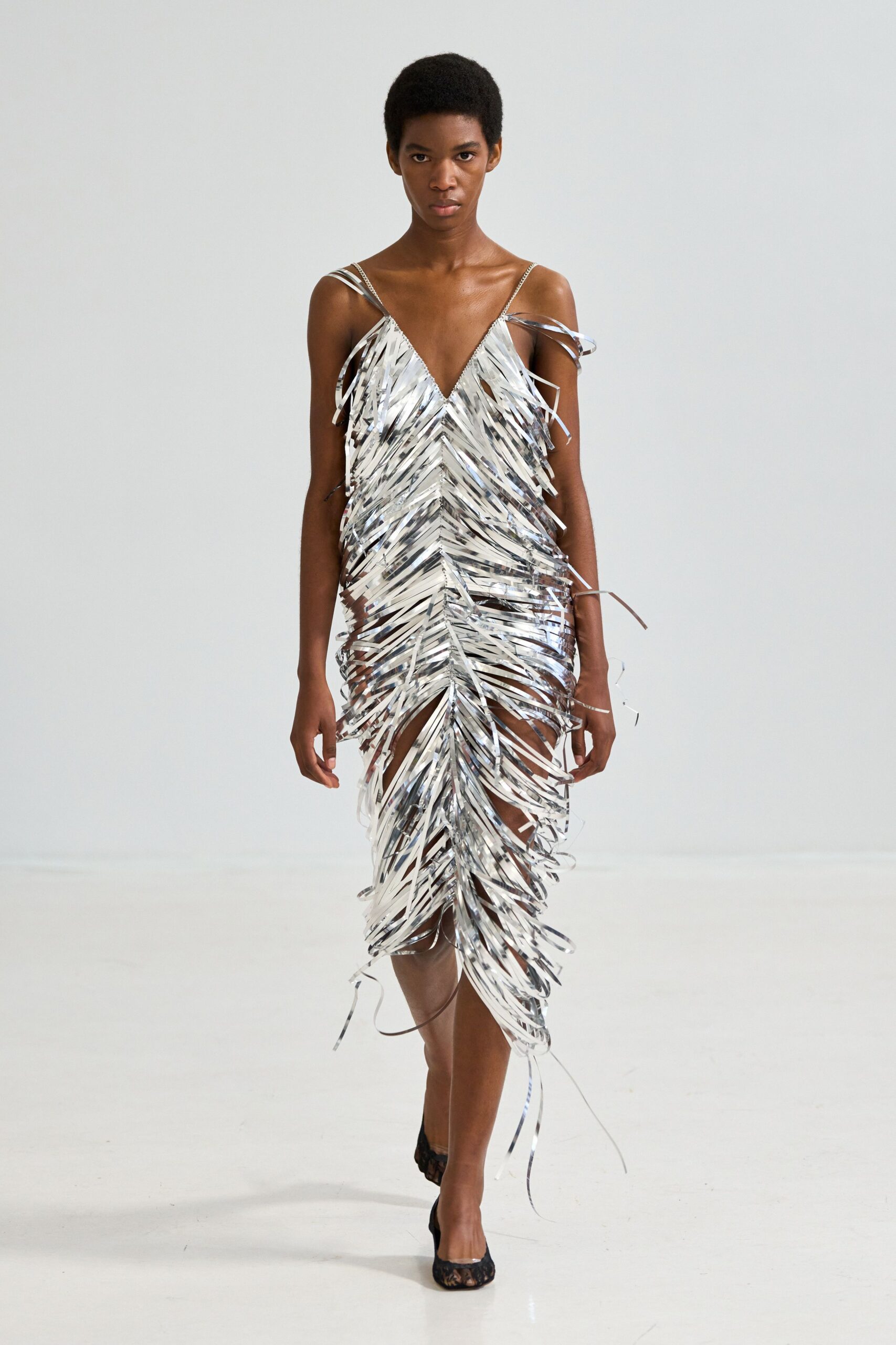 Silver mirror-fringe slip dress, narrow straps and a deep V skimming the body. Black lace pumps peeking out under the tinsel hem. Crossing the hotel ballroom floor after the band has packed up.