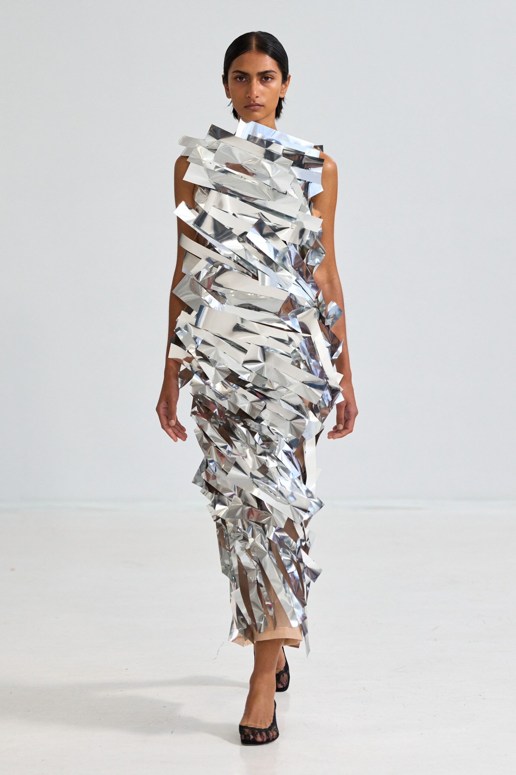 Column dress built from crinkled silver foil strips, one ribbon kicking off the shoulder. Black lace mules with a sheer open toe. Whatever you wear to carry the tinsel down after the party collapsed.