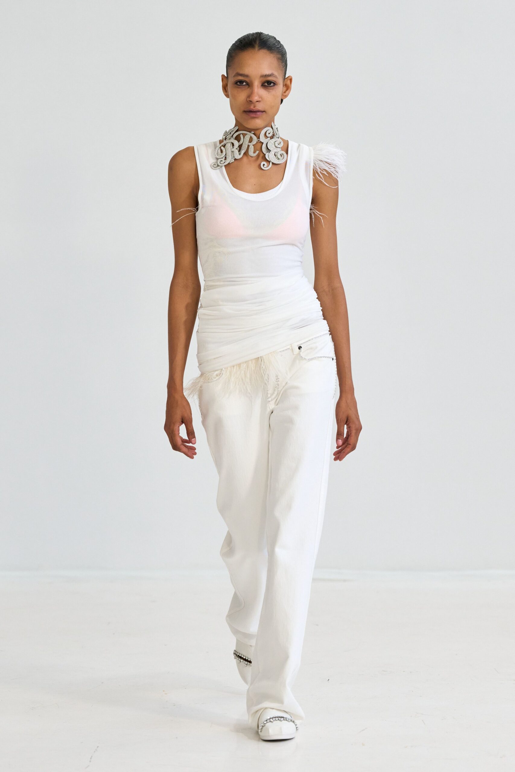 Glittering script-letter collar curling high around the throat. Sheer white rib tank, ruched through the waist with feather tufts. Loose white trousers, a silver chain drooping from the pocket edge. Square white flats banded with pearl-like studs. Walking into a registry office with confetti still caught on your shoulder.