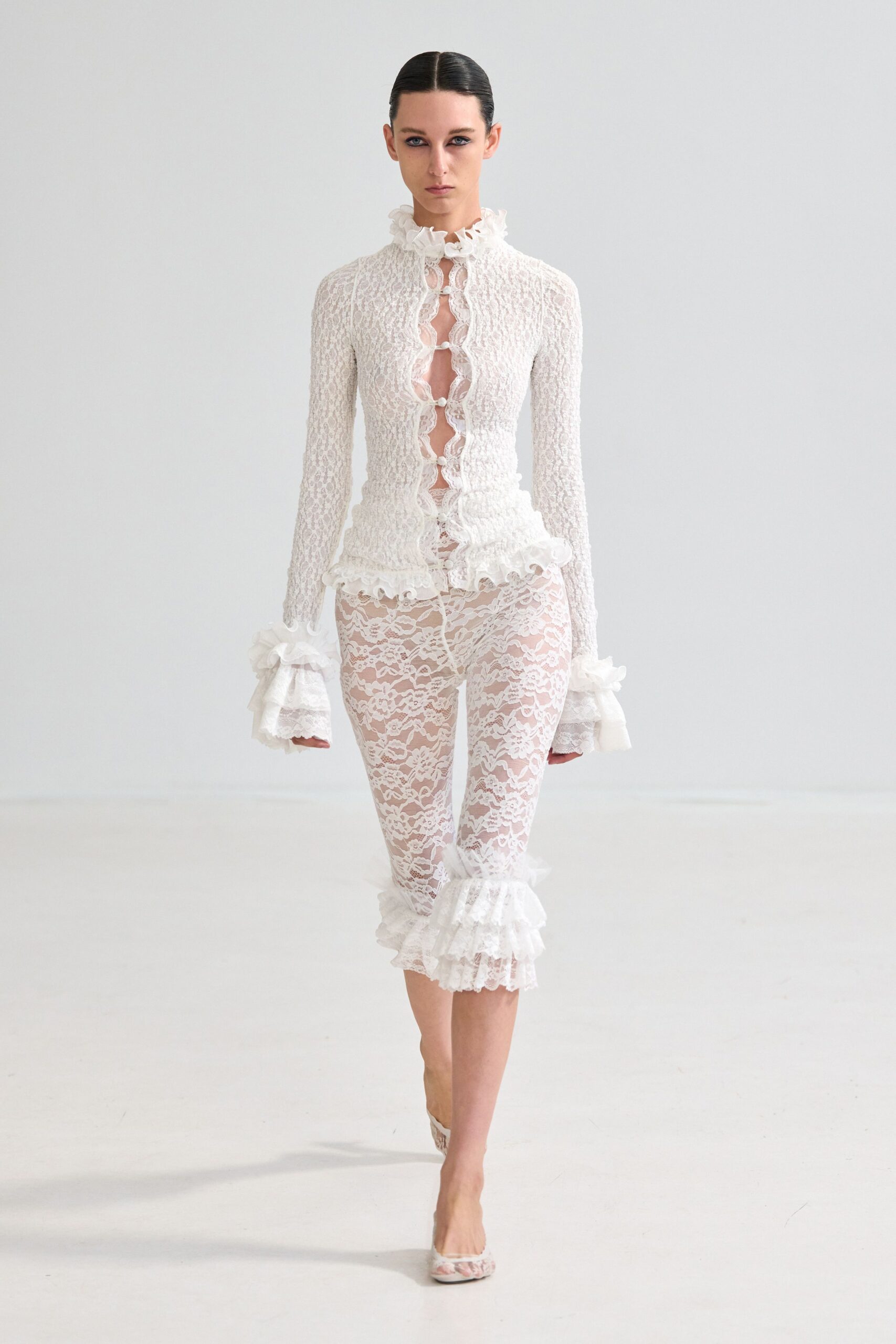 Ivory lace top with a ruffled stand collar and looped open placket. Sheer floral lace leggings, one calf finished with a tiered flounce. Open-toe lace mules. Registry office stairs, carrying your shoes before the rice hits.