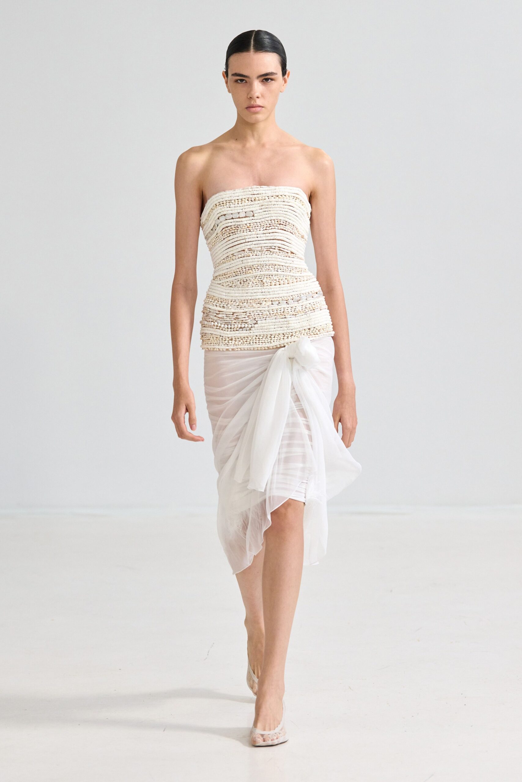 Ivory corded bands packed with pebble-like knots and tiny open ladders. Sheer white chiffon ruched tight, tied in a swollen hip knot. Pale mesh pumps with a lace-edged pointed toe. Registry office at noon, bouquet still in the sink upstairs.