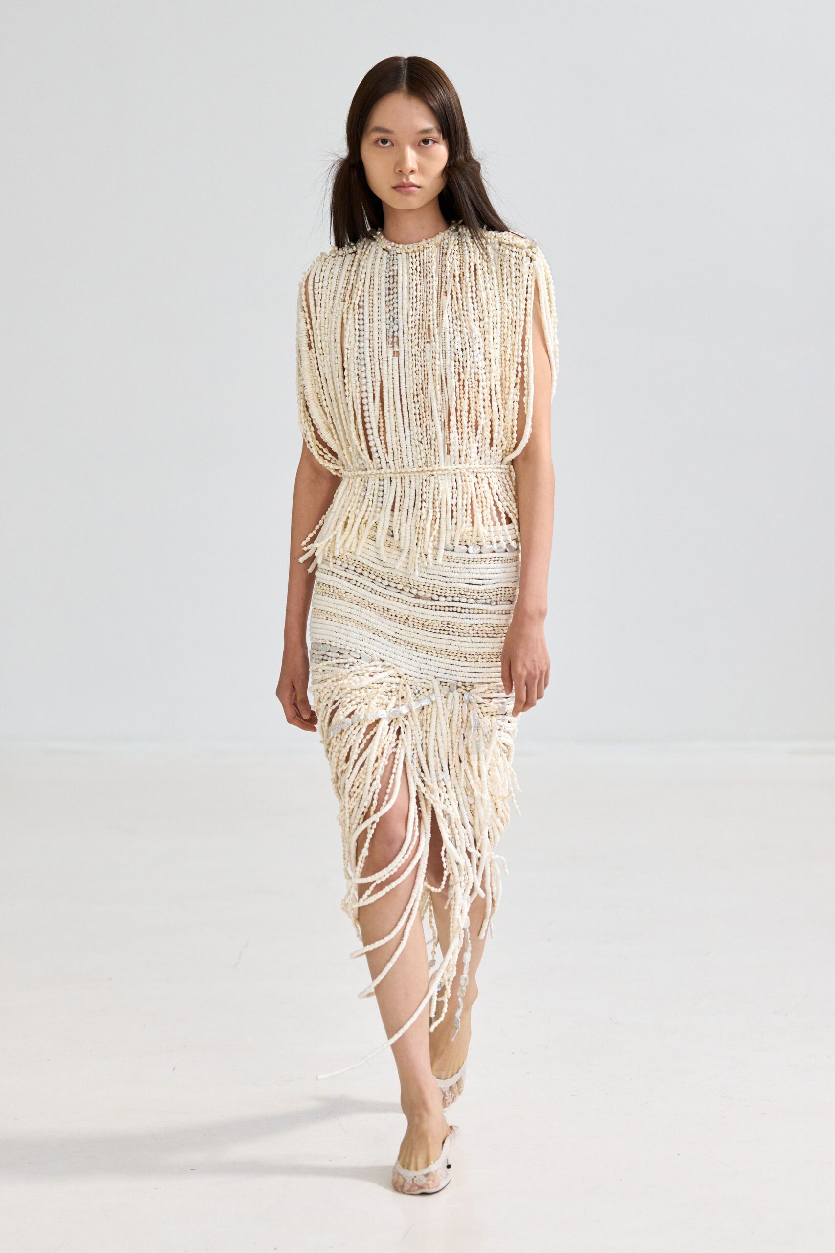Ivory beaded fringe top, cap sleeves dissolving into dangling cords. Matching beaded skirt, ruched at the thigh with looping strands. Pointed mules in pale brocade. Walking barefoot home from a beach wedding, shoes dangling by two fingers.