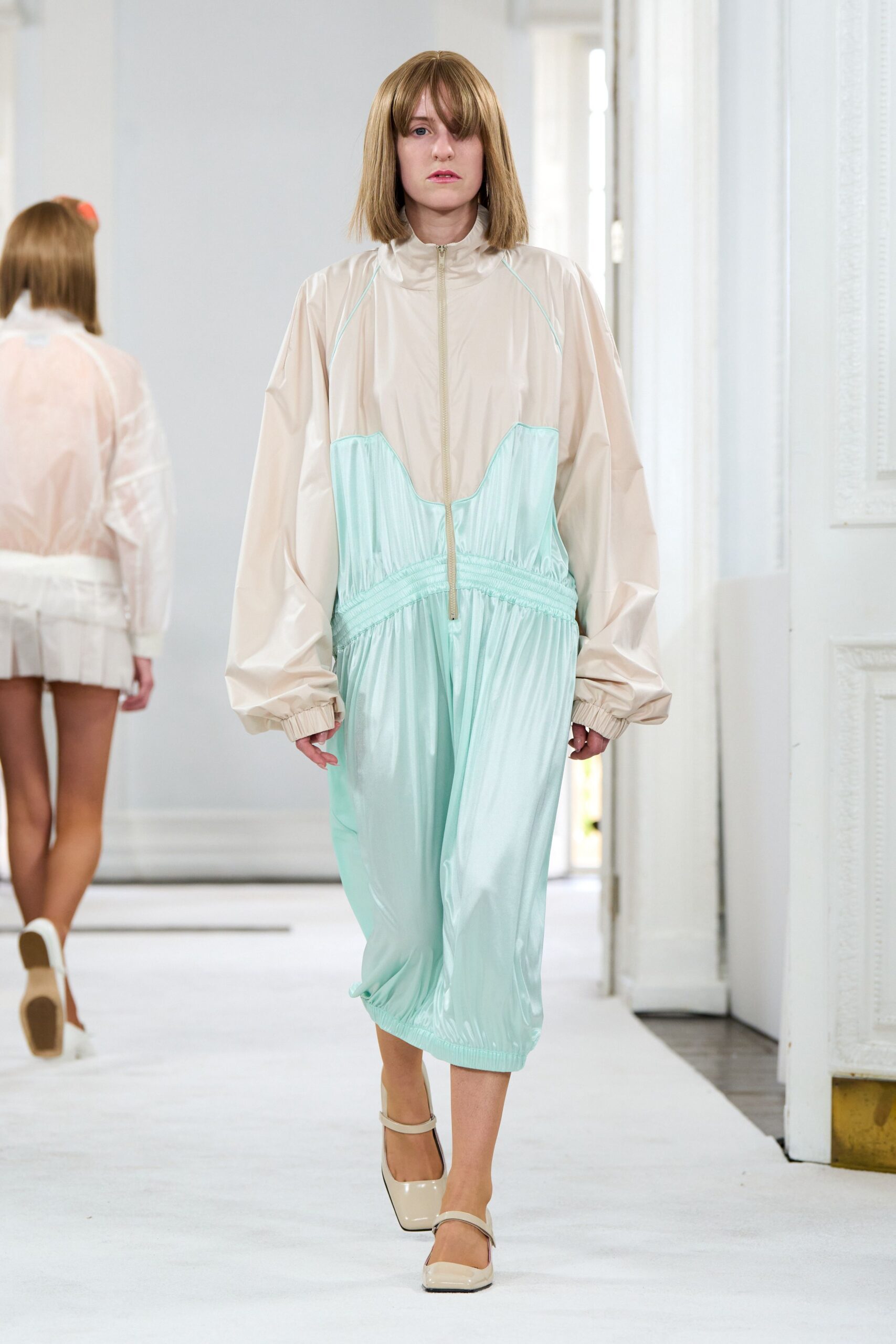 Cream nylon zip-front jumpsuit spliced to a mint gathered lower half. Balloon sleeves with tight elastic cuffs. Square-toe cream Mary Janes with a narrow strap. Walking the hotel corridor before breakfast, hair still bent from sleep.