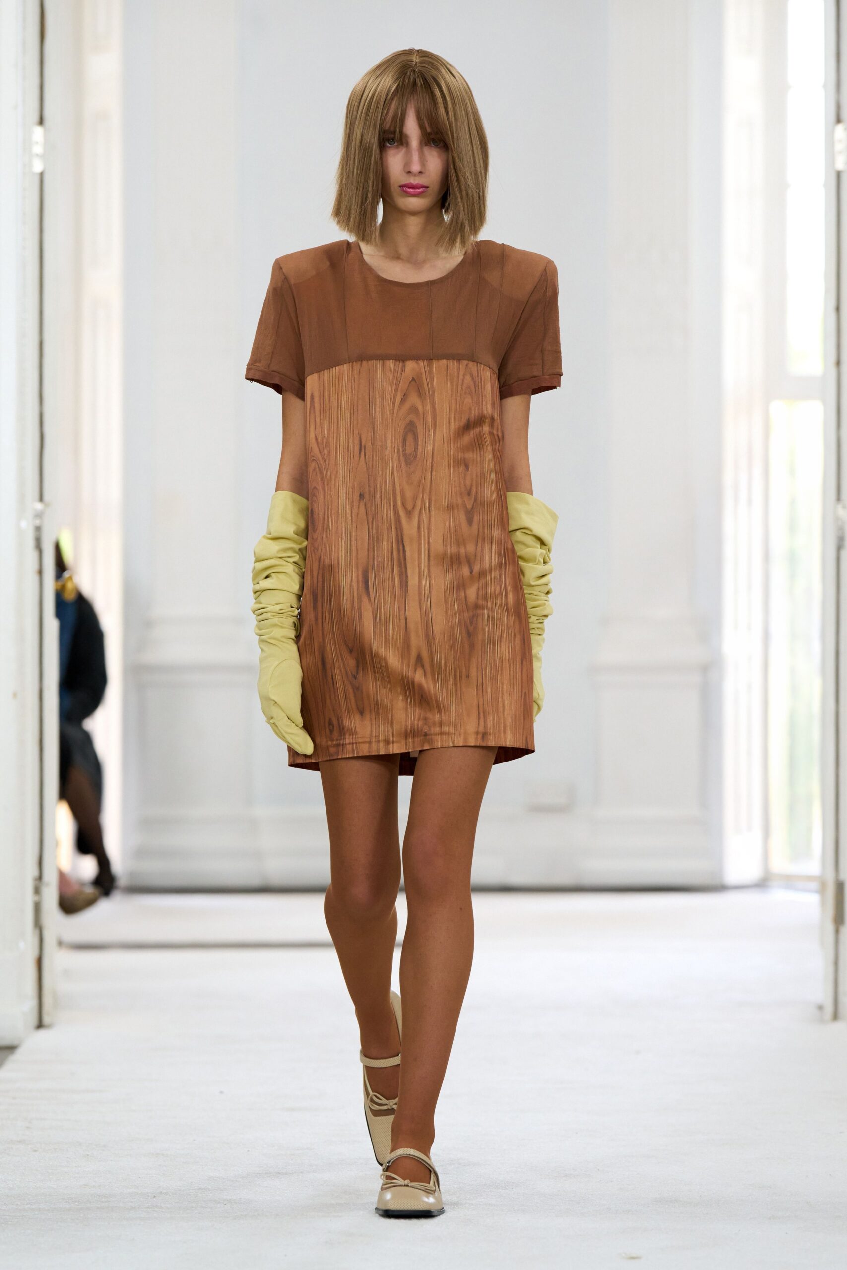 Brown shift mini with trompe l'oeil woodgrain front and padded shoulders. Pale chartreuse opera gloves, ruched down the forearms. Cream ballet flats with a tiny bow and square toe. Walking through an empty house before the varnish smell has gone.