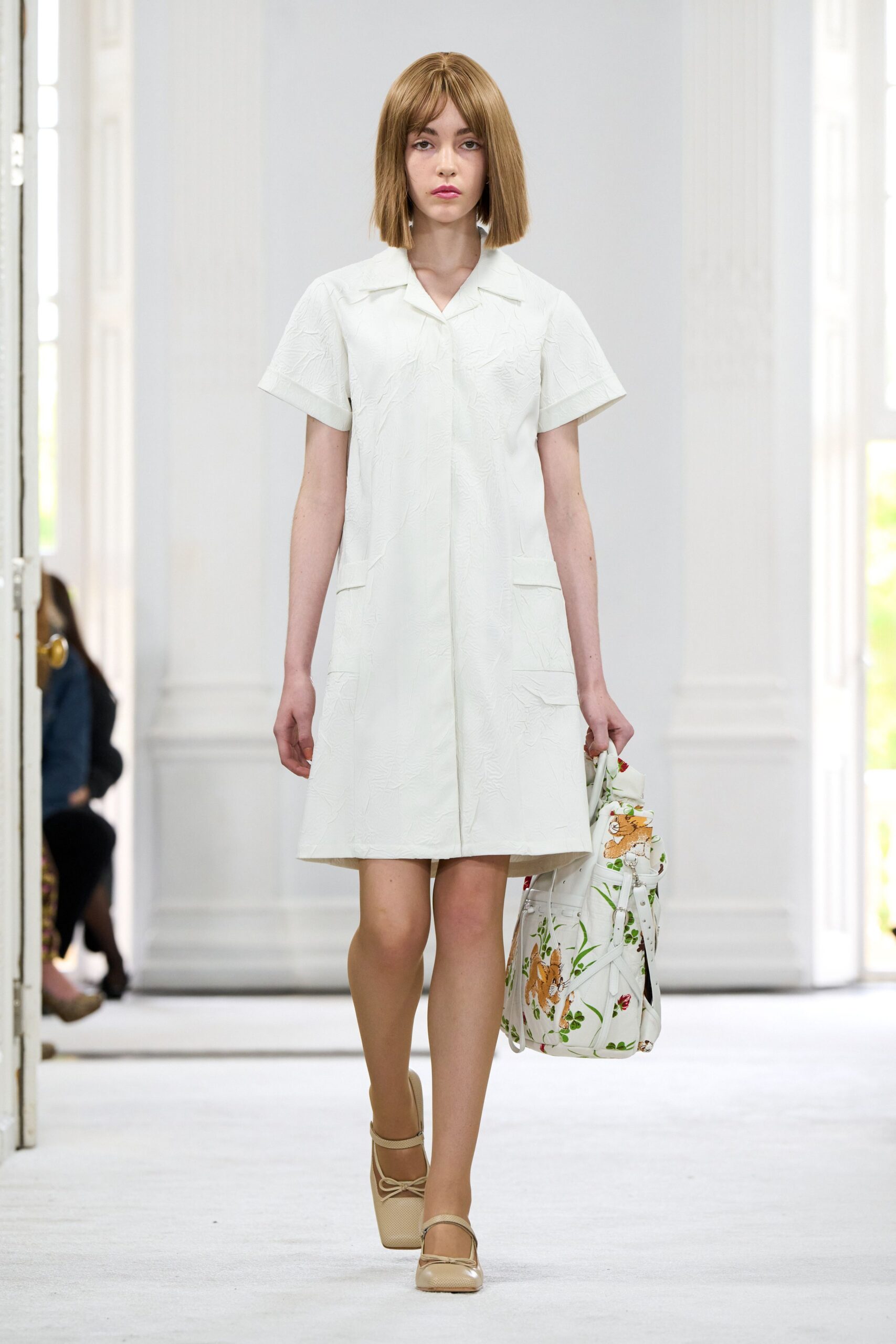 Cream shirt dress in crinkled jacquard, patch pockets set low at the hip. White bucket bag printed with rabbits and trailing green stems. Biscuit leather Mary Janes with a square toe and tiny bow. For bringing pastries through a hotel corridor before everyone else is awake.