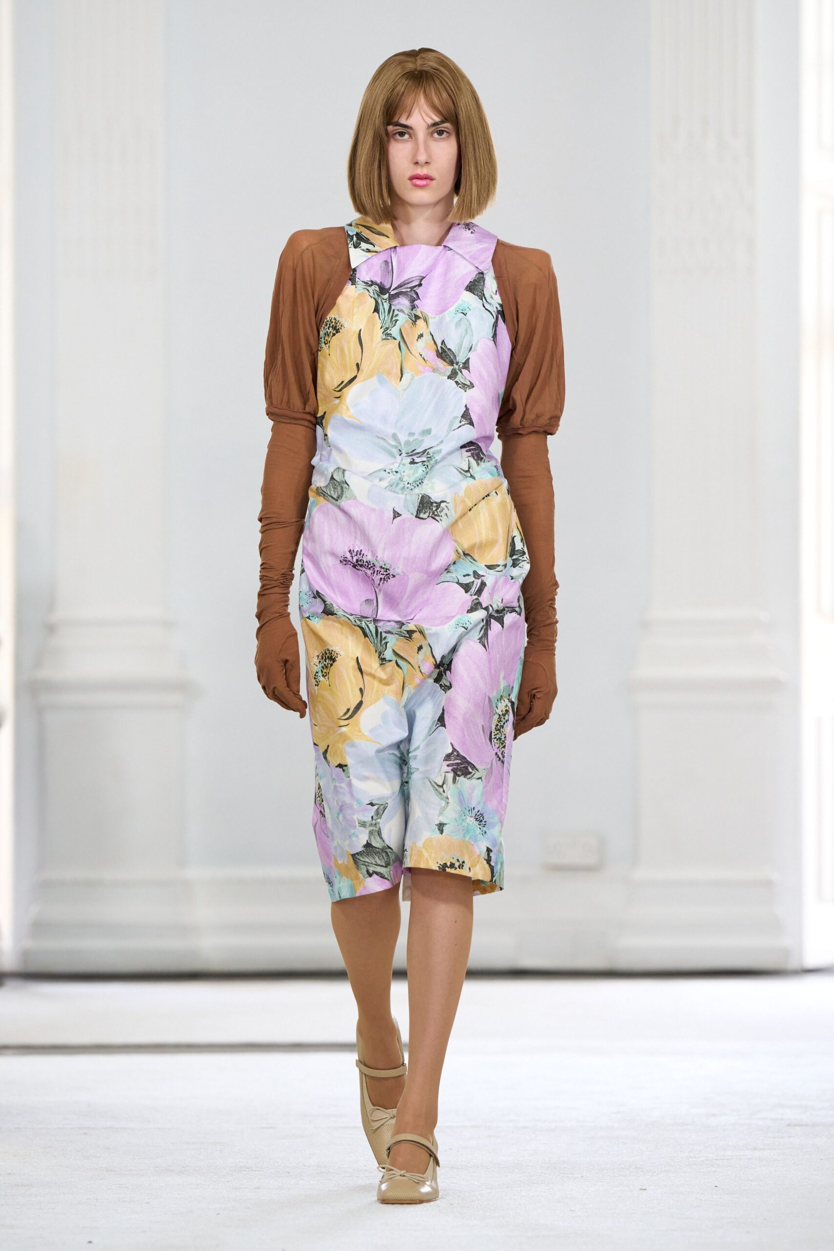 Pastel floral jumpsuit with a folded bib neckline and loose draped hip. Cinnamon jersey gloves extending past the elbows, lightly ruched at the wrists. Beige mesh Mary Jane heels with a small bow at the toe. Walking through a conservatory after the flower show has already closed.