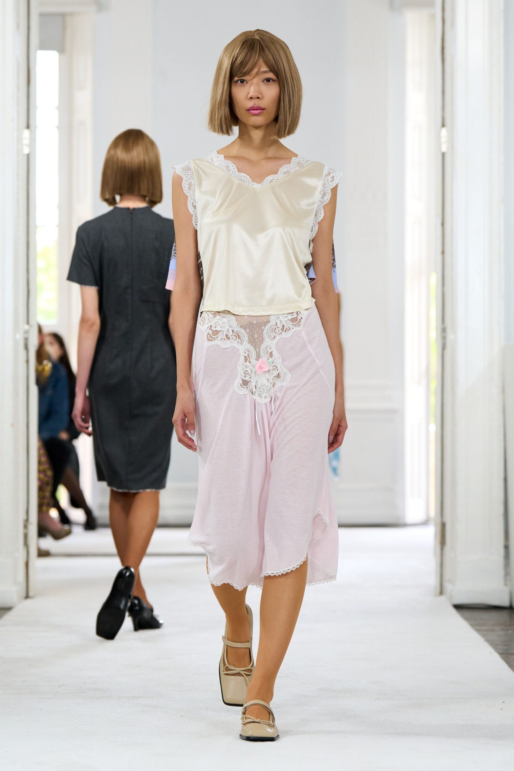 Ivory satin camisole with scalloped lace edging the V-neck and armholes. Powder-pink jersey slip skirt, lace yoke dropping to a tiny rosette drawstring. Cream mesh Mary Janes with square toes and doubled bow straps. Sunday morning in a rented apartment, coffee cooling on the sill.