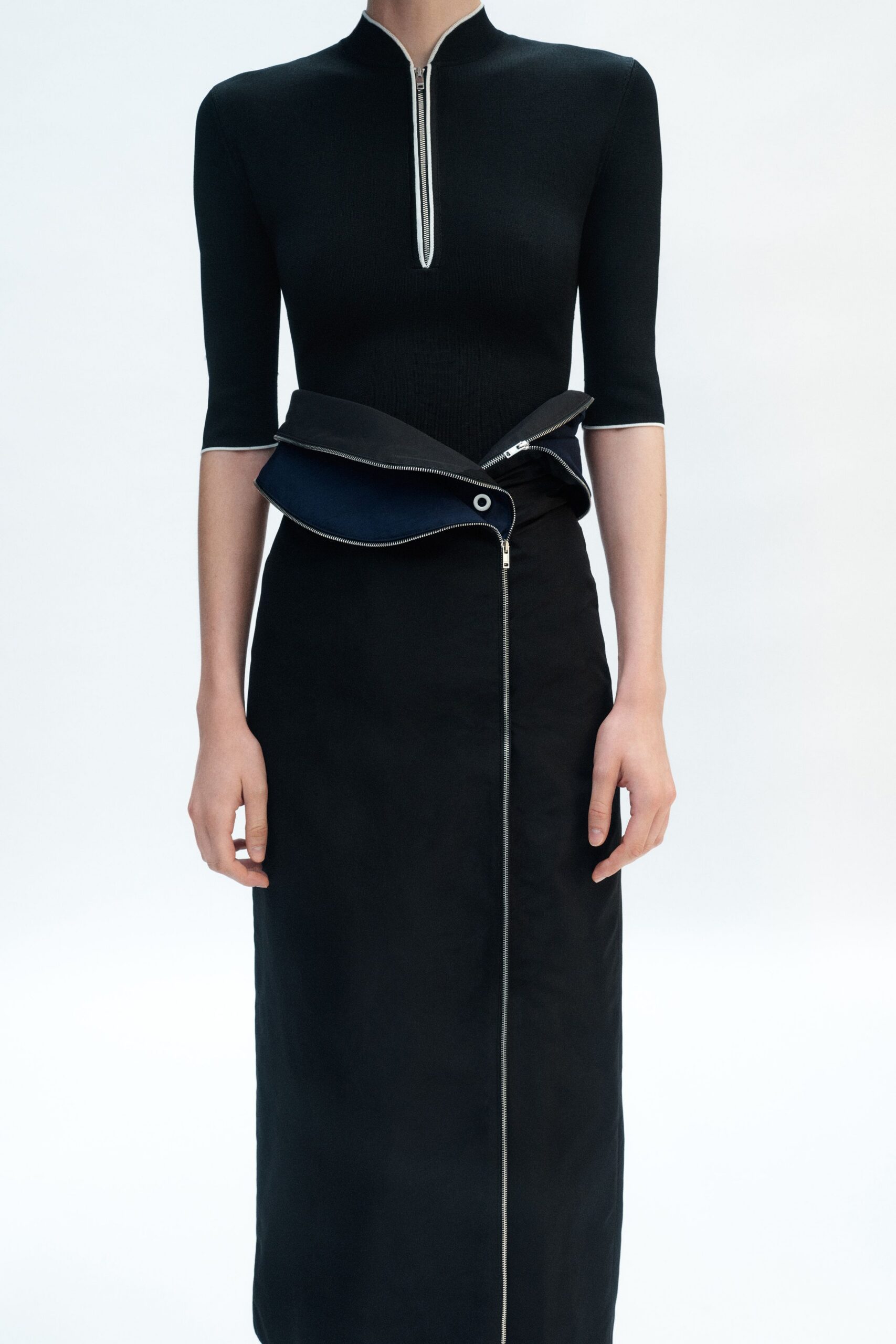 Black rib knit top with white piping and a half zip. Black midi skirt split by a vertical zip, waistband folded open to navy lining. For the train ride back from a design fair with one brochure left.