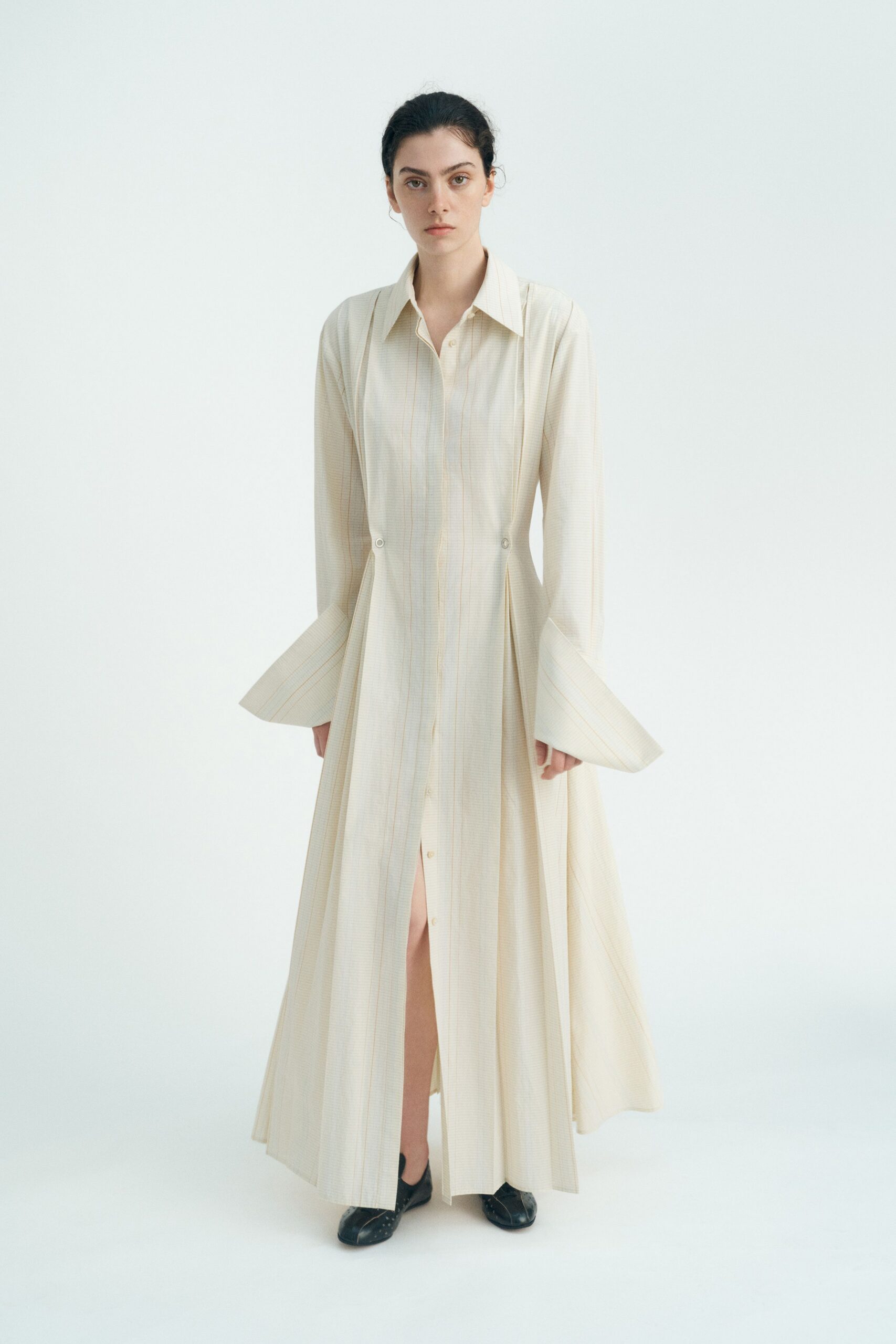 Cream microcheck shirt dress with pinched waist and long bell cuffs. Black square-toe flats, tiny studs catching at the vamp. Sunday museum hush, the heating still not switched off for spring.
