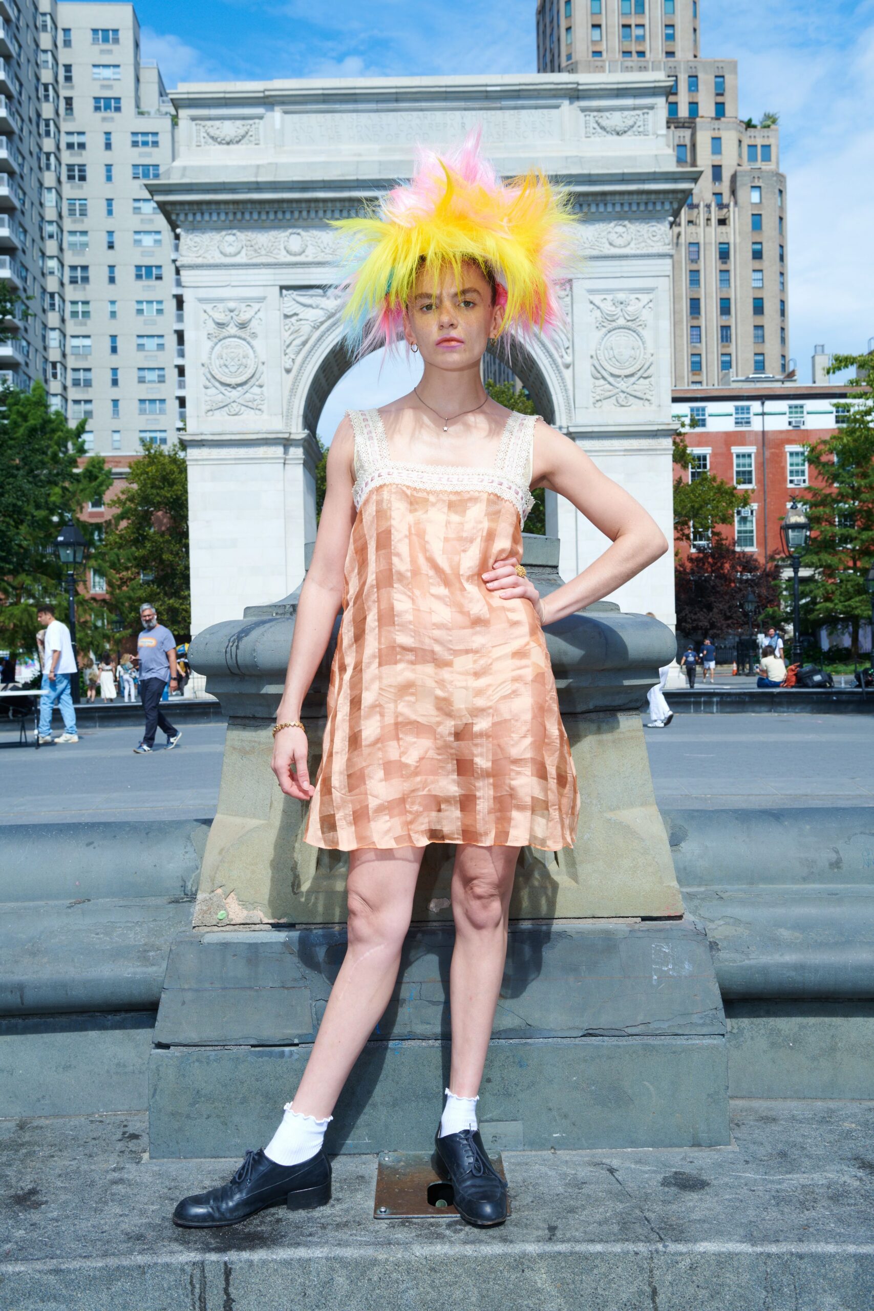 Spiked neon wig in lemon, pink and mint synthetic fluff. Peach shift dress in crinkled checker satin with cream crochet straps. Tiny pendant on a black cord. White ankle socks with lettuce edges. Black lace-up shoes, one toe lightly scuffed. Noon by the fountain, tourists circling while your hair catches every gust.