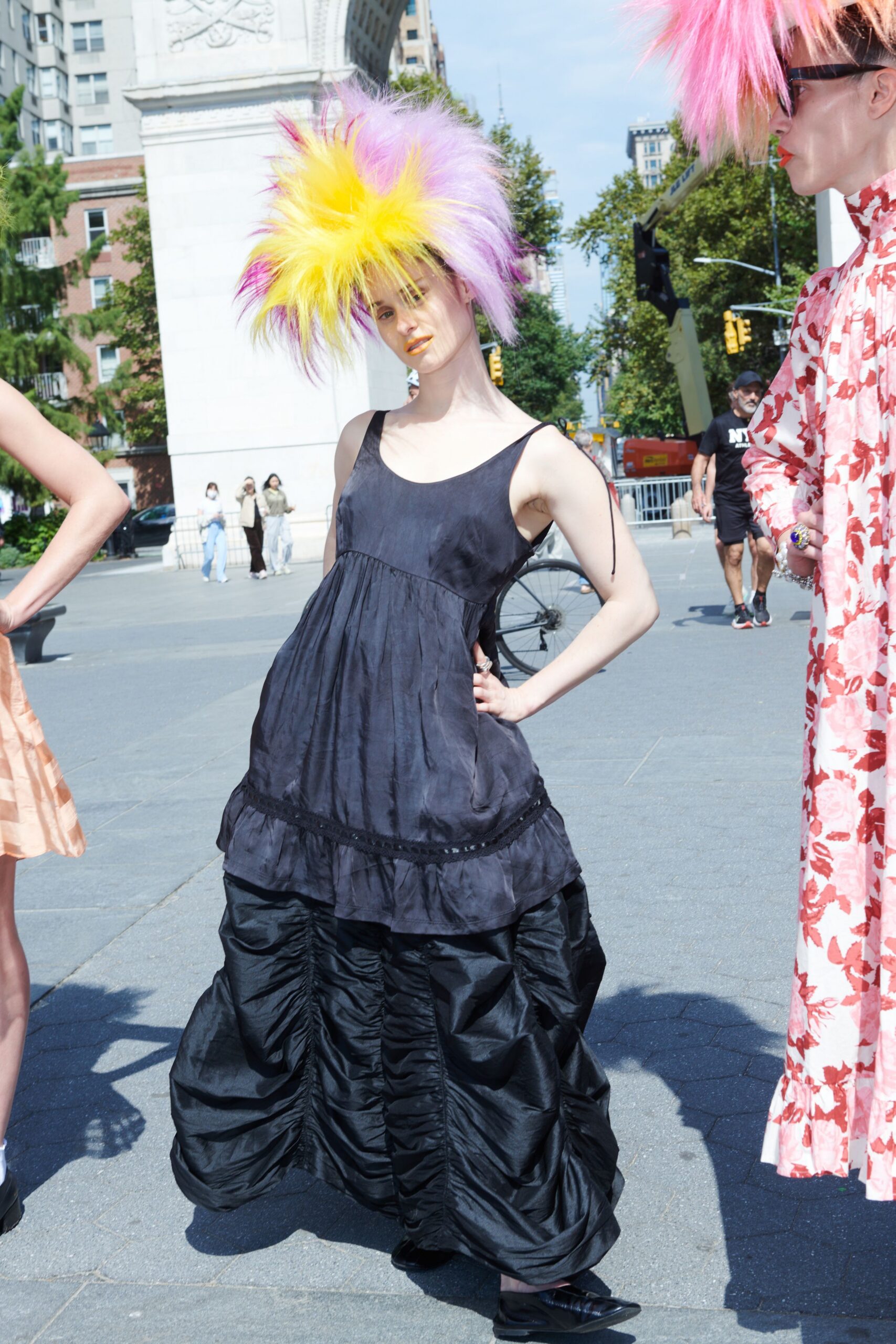 Spiked faux-fur hat in lemon, lilac and hot pink. Black satin slip bodice falling into a dropped lace-trim flounce. Pooled black taffeta skirt, vertically ruched into inflated channels. Pointed black flats with a low vamp. Crossing the square after noon, dressed louder than the fountain.