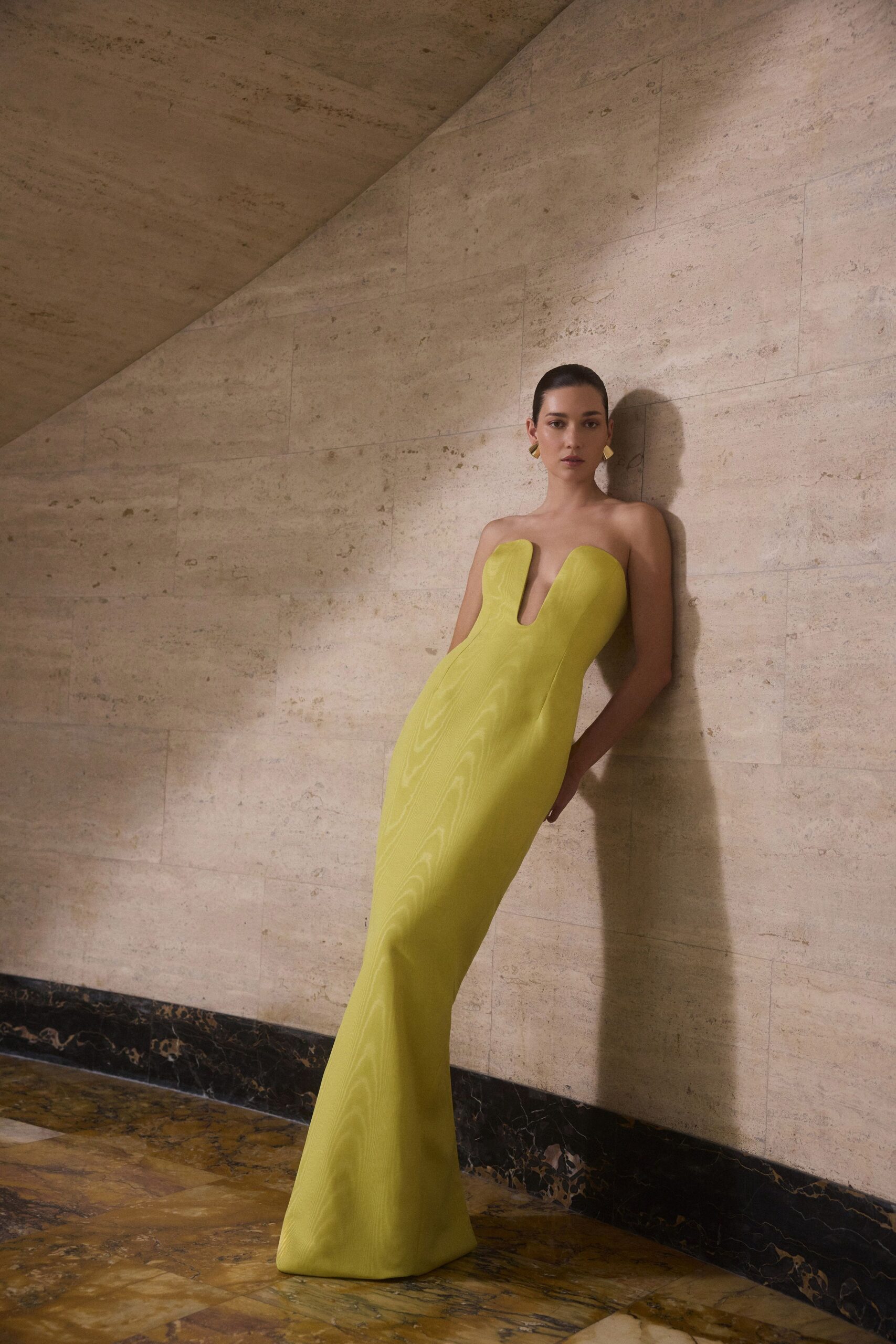 Chartreuse strapless column gown with a plunging U notch and moire shimmer. Small folded gold earrings. Museum stairwell hush, just before the benefit doors open.