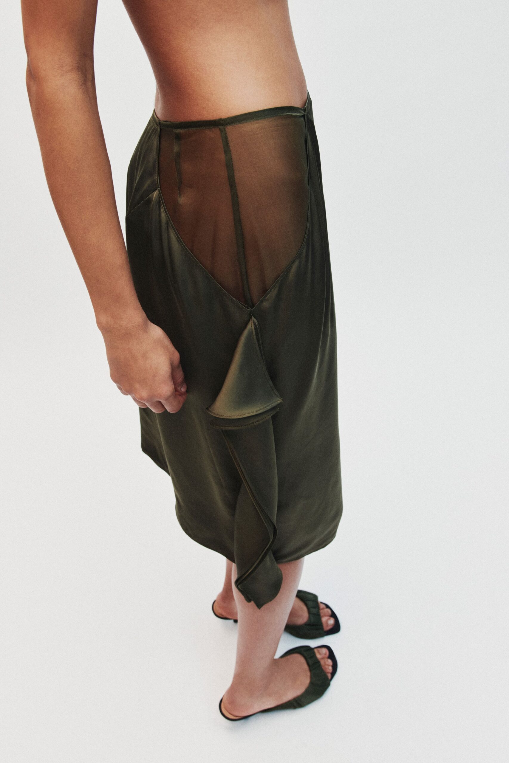 Olive satin midi skirt with a sheer mesh side panel and drooping ruffle. Dark green ruched mules with narrow black soles. For crossing a hotel corridor barefoot in everything but the shoes.