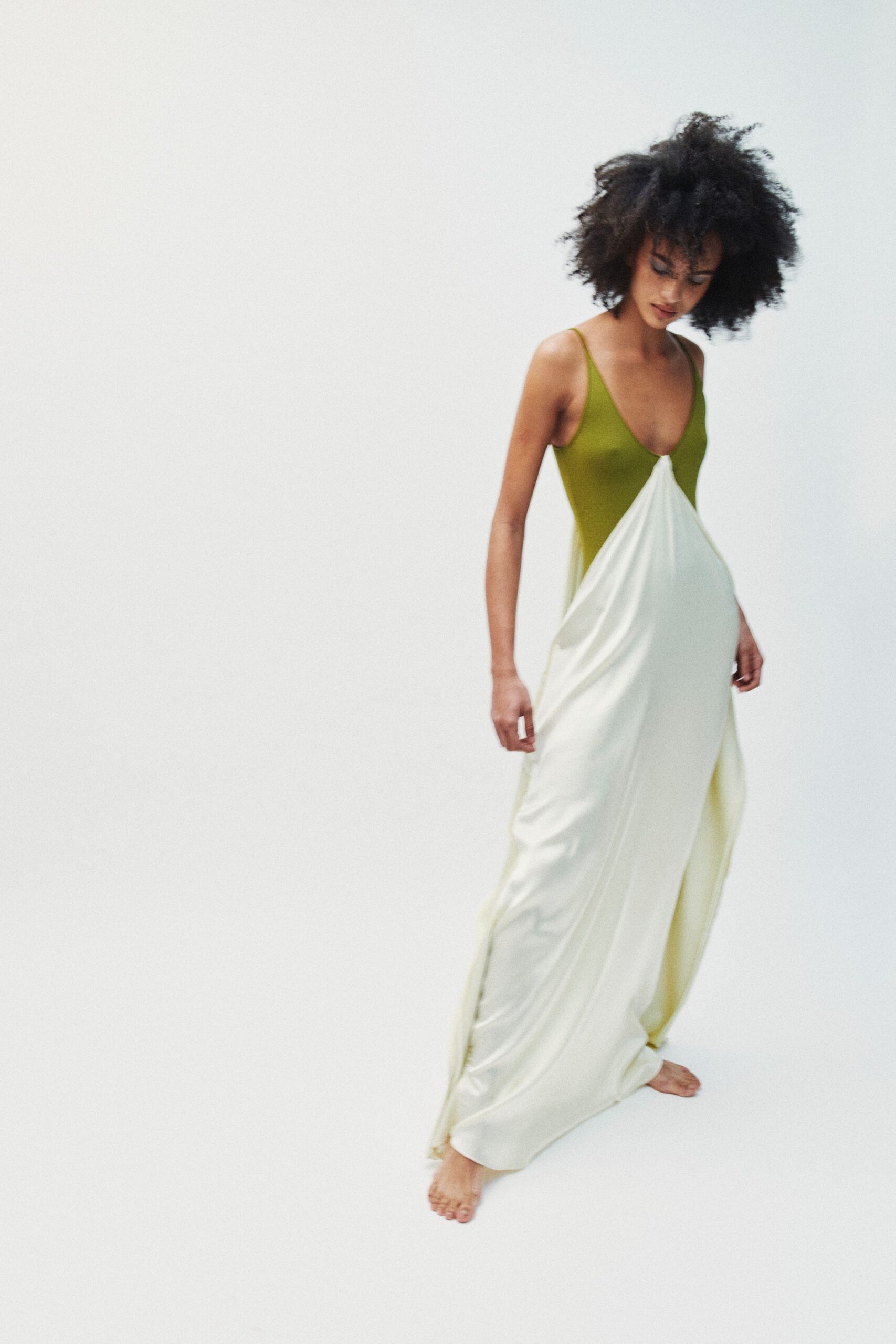 Moss green bodice with needle straps and a plunging scoop front. Ivory jersey falls from the center bust in a long gathered sweep. No shoes, hem nearly skimming the toes. Early checkout, hotel robe forgotten and the sheet improvised into evening.