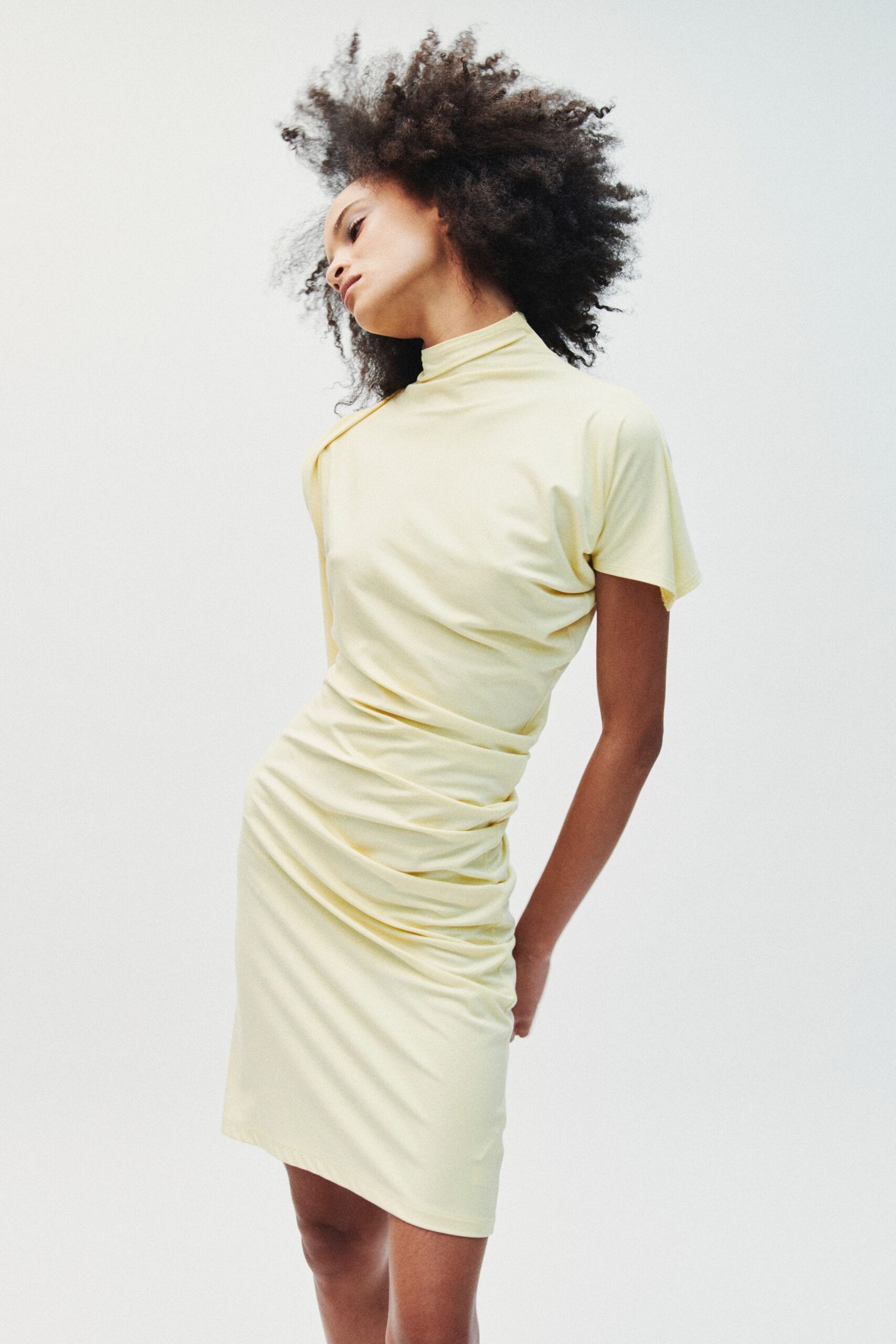 Pale butter jersey dress with a rolled mock neck and side ruching. The first warm Sunday when the city still smells faintly of laundry steam.