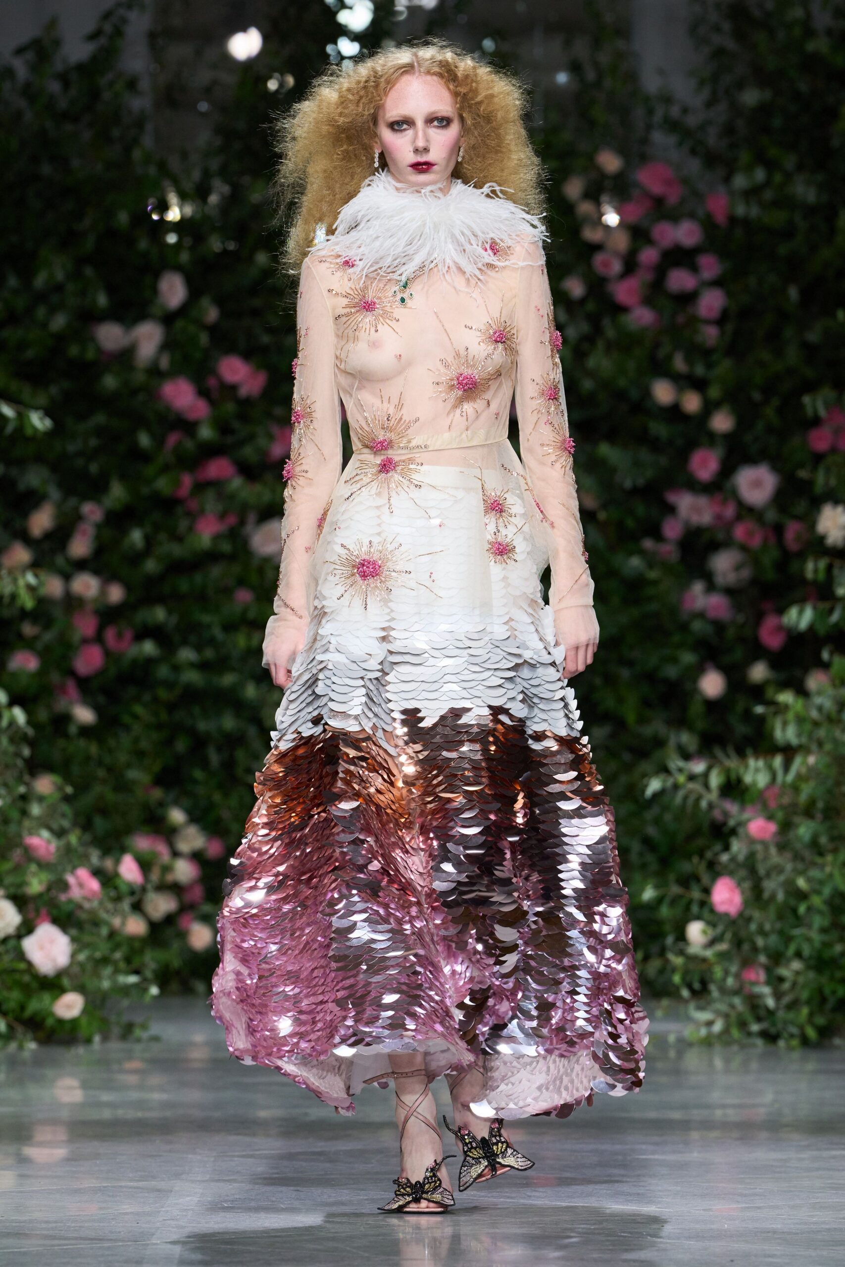 Short crystal drop earrings. White feather collar flaring soft around the throat. Nude illusion bodice with pink beaded starbursts and a petal paillette skirt fading to rose gold. Ankle-tie sandals topped with beaded butterfly wings. In a glasshouse after rain, roses breathing against the warm panes.