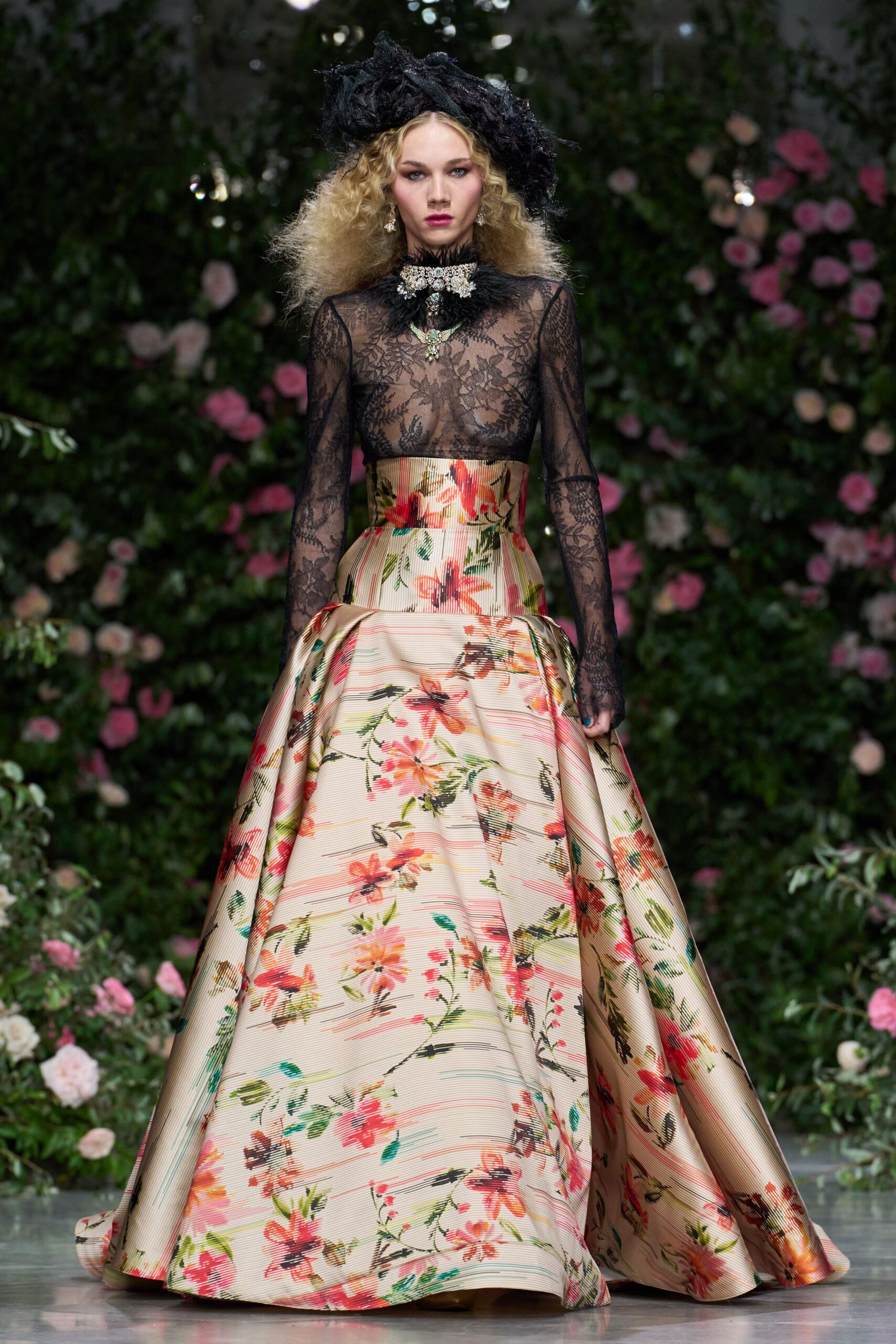 Black crumpled tulle hat, tilted wide over blown-out curls. Sheer black floral lace with a spiky eyelash collar. Crystal cluster choker over black feather trim. Champagne faille skirt printed with blurred garden blooms, dropped pannier hips. For arriving at a winter wedding after rain, hem already grazing wet stone.