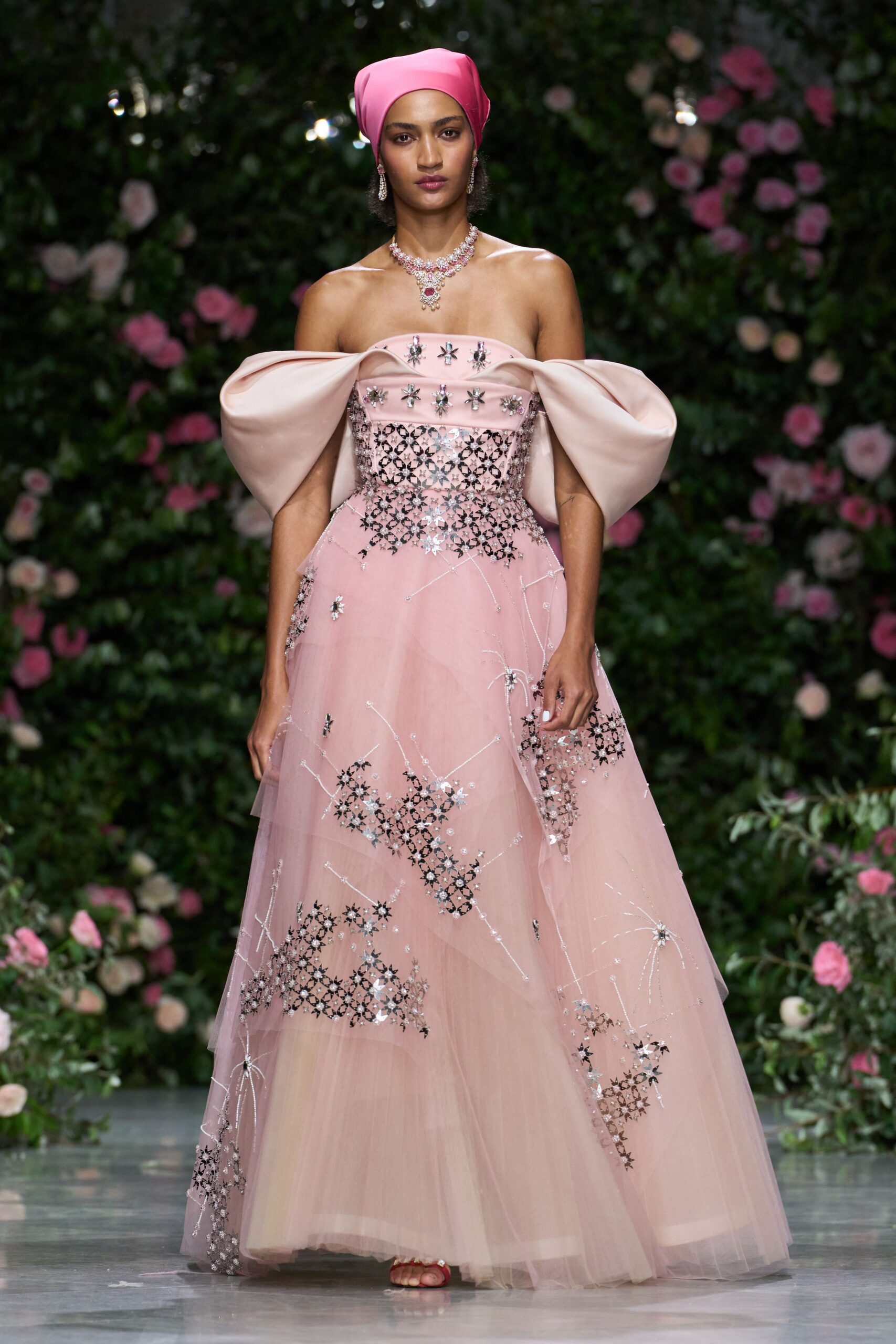 Bubblegum satin headscarf folded close over the crown. Blush tulle ballgown with mirrored starbursts and outsized bow sleeves. Pink jeweled thong sandals peeking from the hem. Garden wedding after midnight, the cake roses already starting to slump.