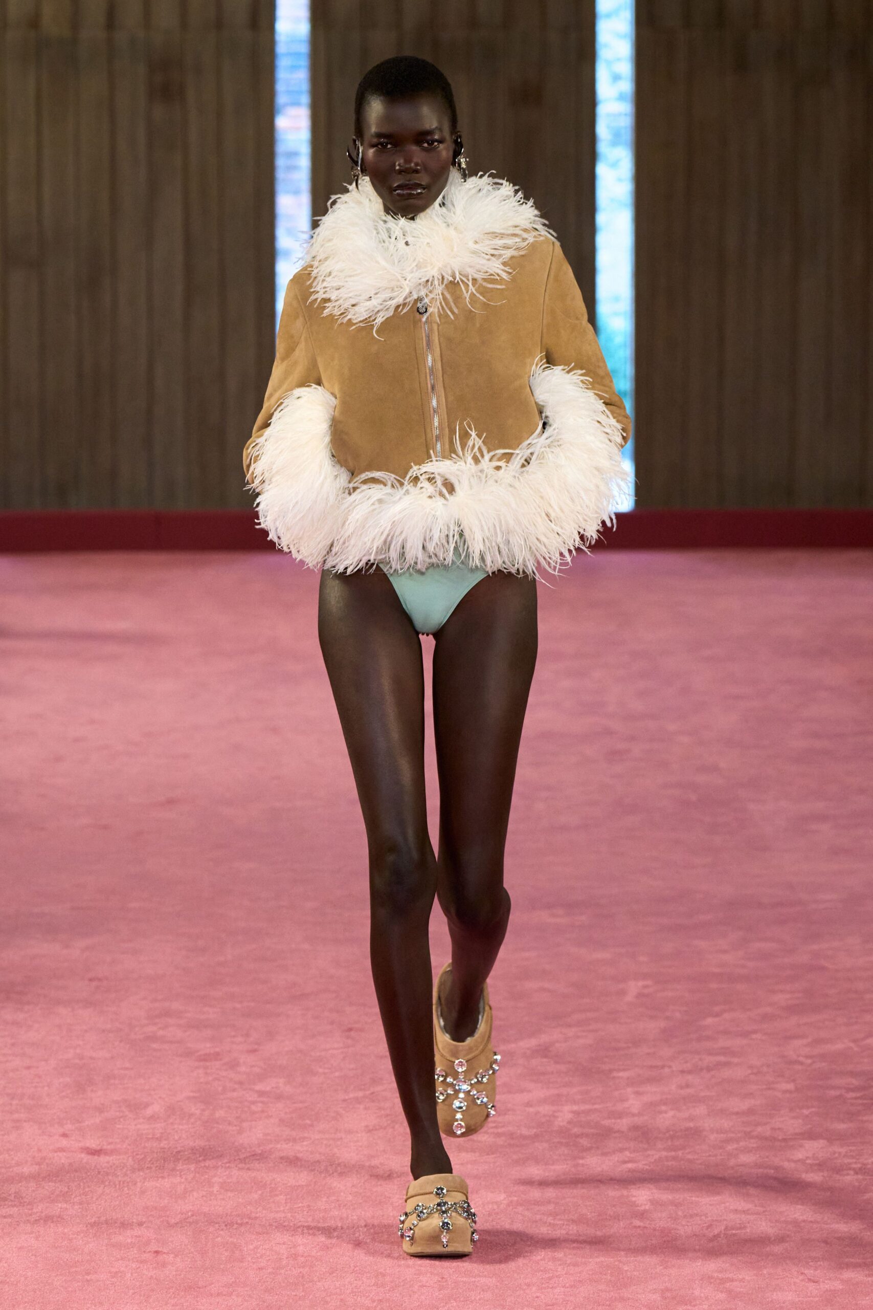 Camel suede jacket zipped straight up, ringed with long white feather trim. Pale mint high-cut briefs, nearly swallowed by the jacket hem. Camel suede mules latticed with crystal flower straps. Hotel corridor at dawn, still wrapped in the duvet and wearing the party shoes.