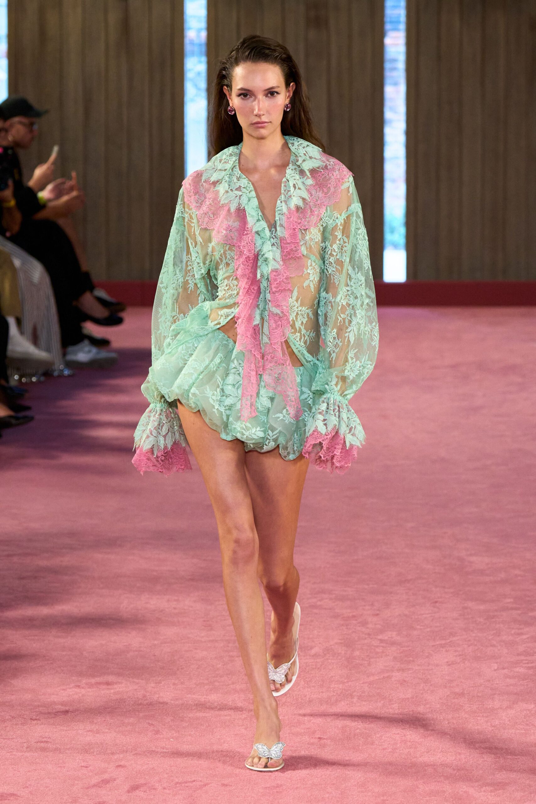 Mint sheer lace blouse with pink ruffled panels falling from the deep V. Matching mint lace bubble shorts, gathered into a puffed hem. White thong sandals with crystal butterfly straps. Hotel courtyard wedding, two glasses of rosé before sunset.