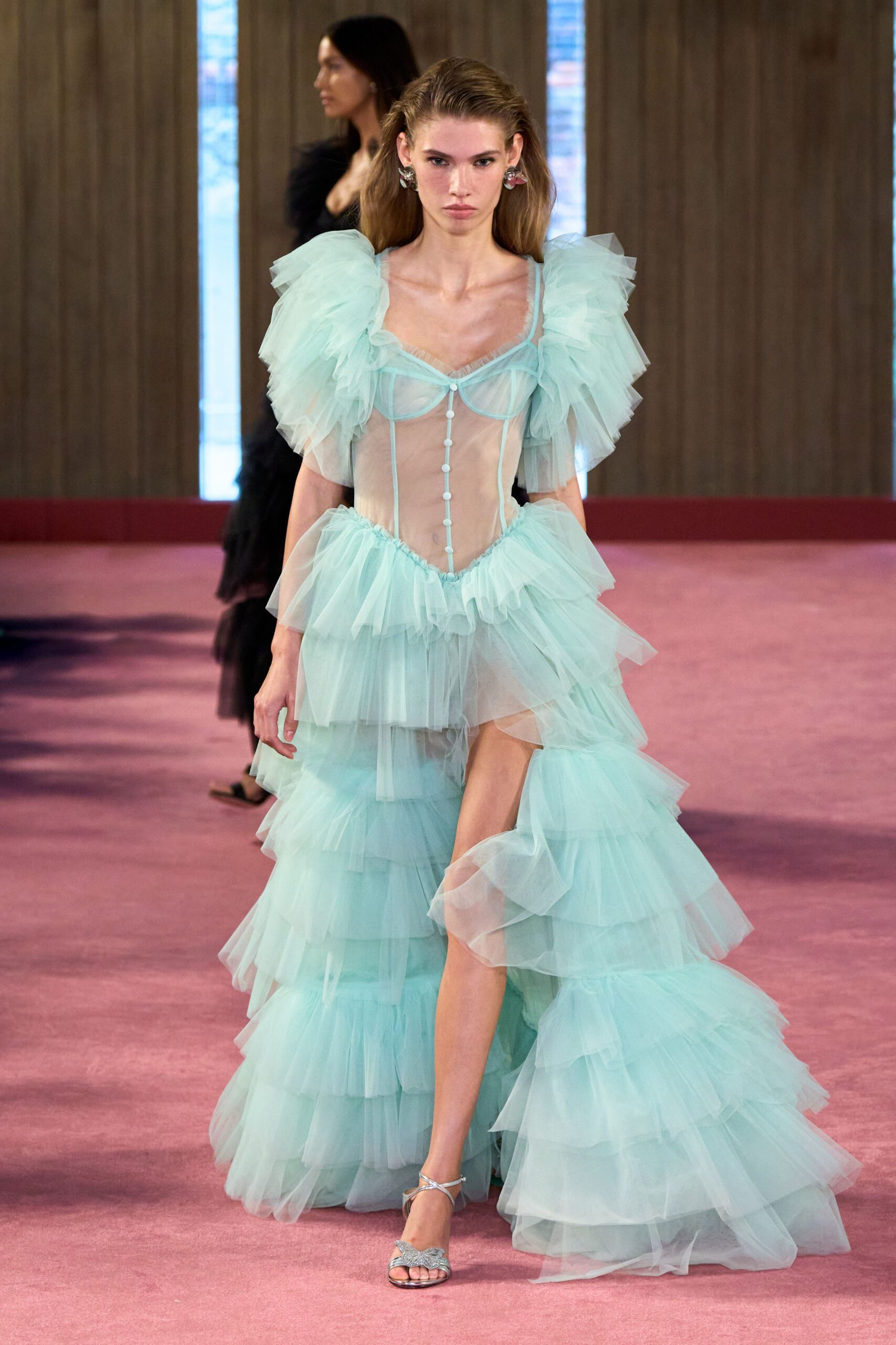 Ice-blue sheer tulle gown with tiered ruffles and puffed shoulder flounces. Shell-like drop earrings flashing pink and silver. Silver ankle-strap sandals with glittered leaf-shaped fronts. Walking across a hotel ballroom carpet after the wedding has thinned out.