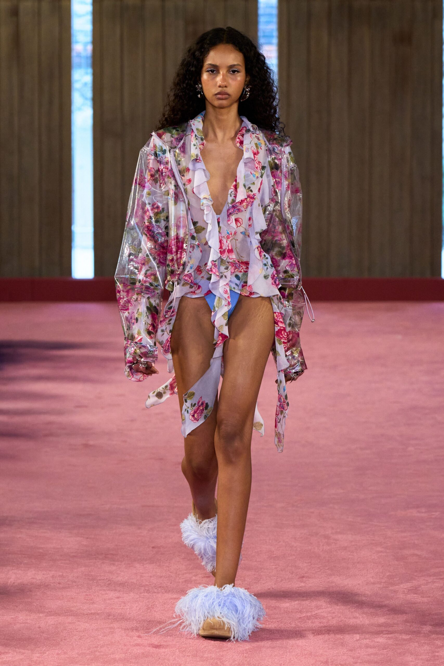 Clear vinyl rain jacket, drawcord cuffs hanging with tiny silver toggles. Lilac floral chiffon blouse, ruffles falling into a deep plunging front. Matching floral briefs with one scarf panel draped off the hip. Powder-blue marabou mules. Walking back from a motel pool with wet hair and nowhere urgent.
