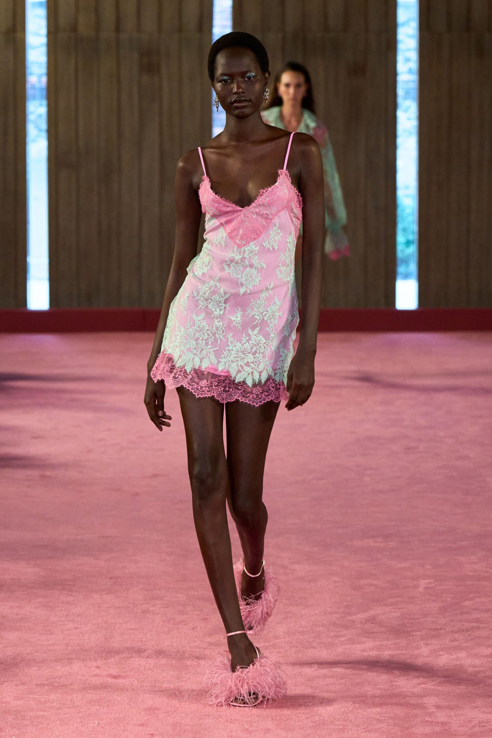 Bubblegum satin slip dress veiled in mint floral lace, scalloped at hem and neckline. Crystal drop earrings. Pink feather-trim sandals with fine ankle straps. Hotel corridor at noon, room service tray still outside the door.
