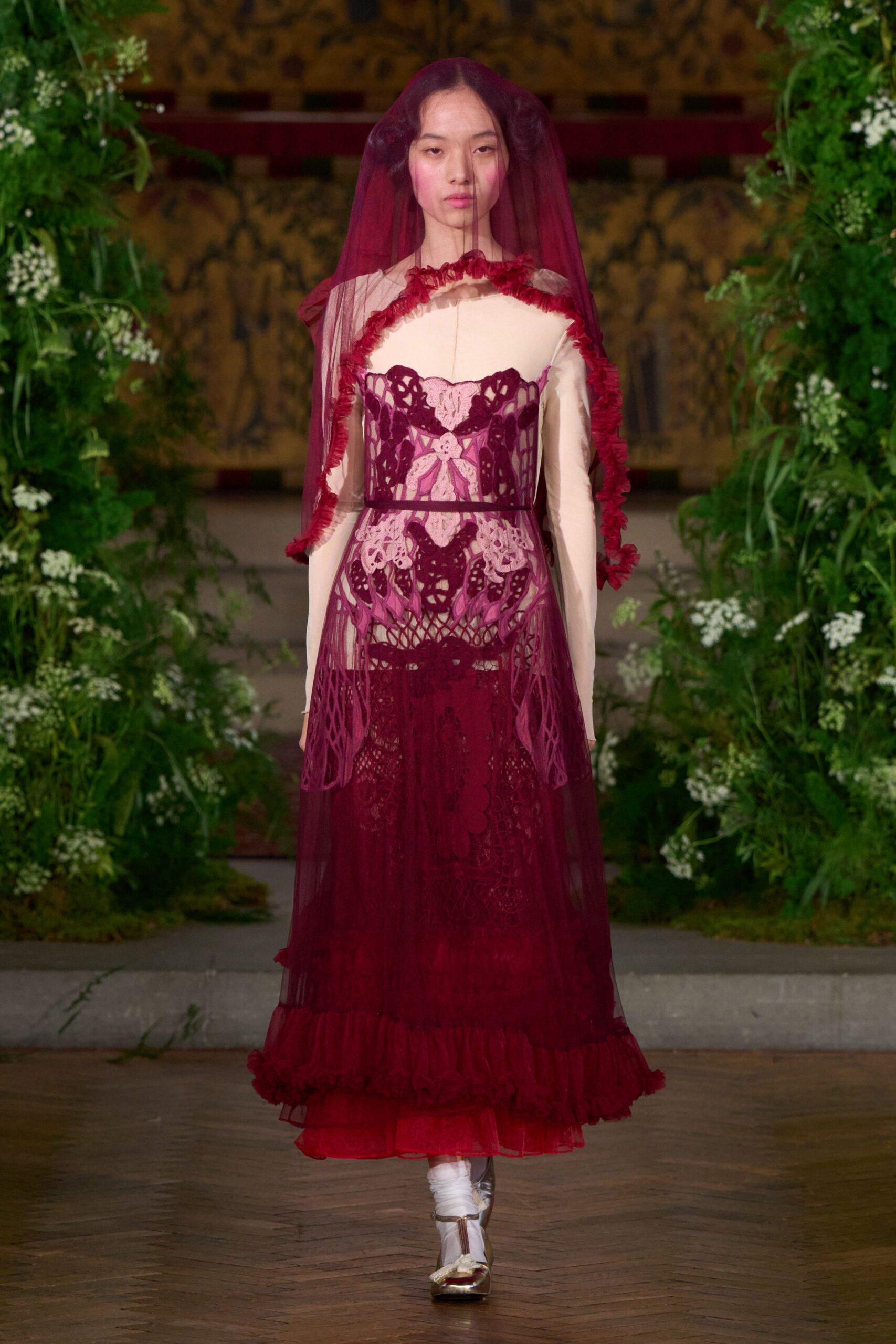 Burgundy tulle veil edged in tight ruffles. Ivory long-sleeve underdress with a stark high neckline. Plum openwork lace and net overlay, cinched with a narrow band. White socks slouched at the ankle. Silver flats with a soft bow across the toe. For a wedding in the walled garden after the grass has gone damp.