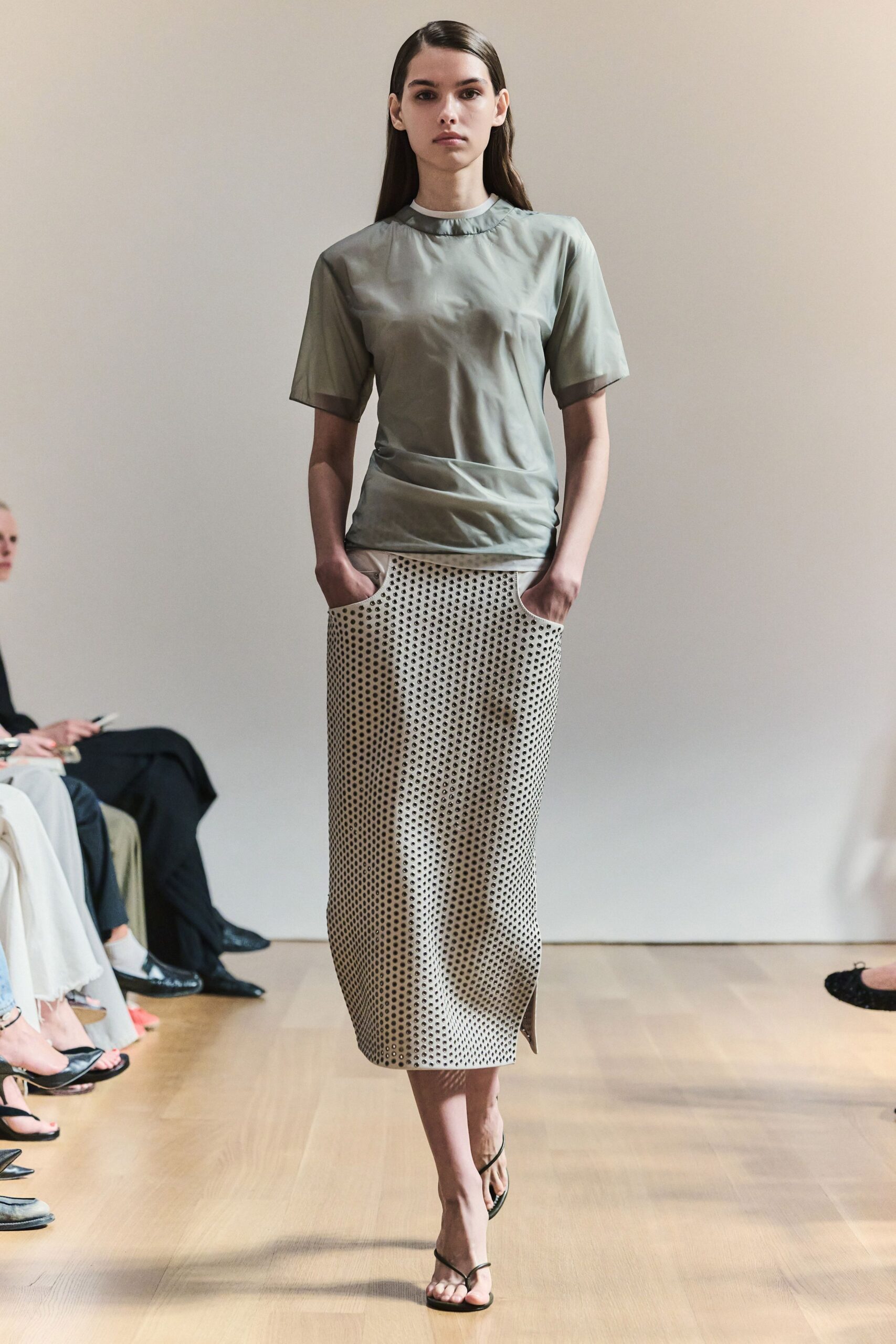 Pale sage satin tee with sheer organza edging at collar and cuffs. Ivory pencil skirt punched all over with tiny black-rimmed eyelets, deep pocket scoops. Bare black thong sandals. Walking across a museum atrium floor just after the rain stops.