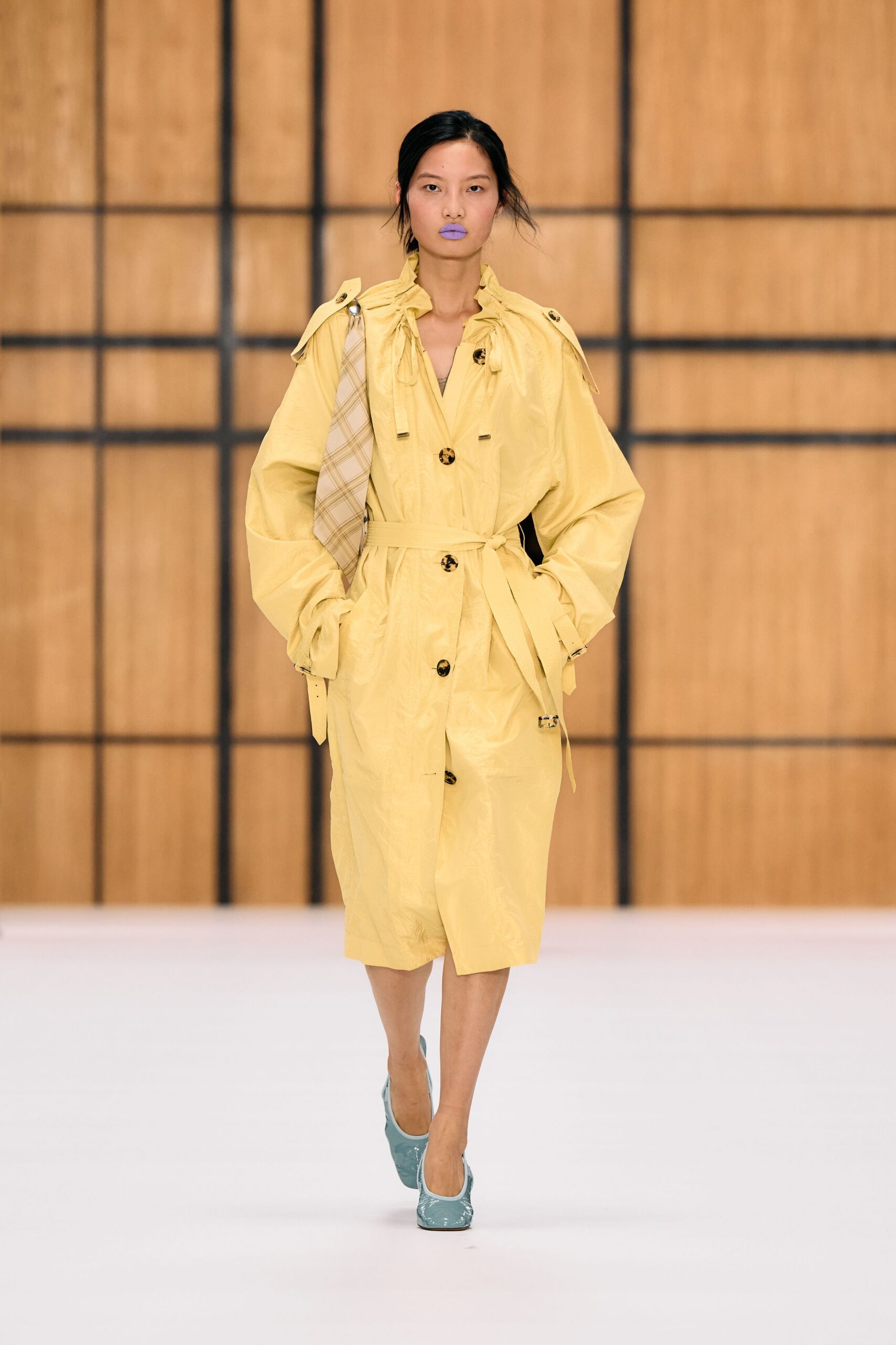Butter-yellow crinkled trench coat with a ruffled drawstring collar and tortoiseshell buttons. Cream plaid tie slung from one shoulder on a silver ring. Powder-blue patent pumps, square at the toe. For crossing a bright hotel lobby with yesterday's conference badge still on.