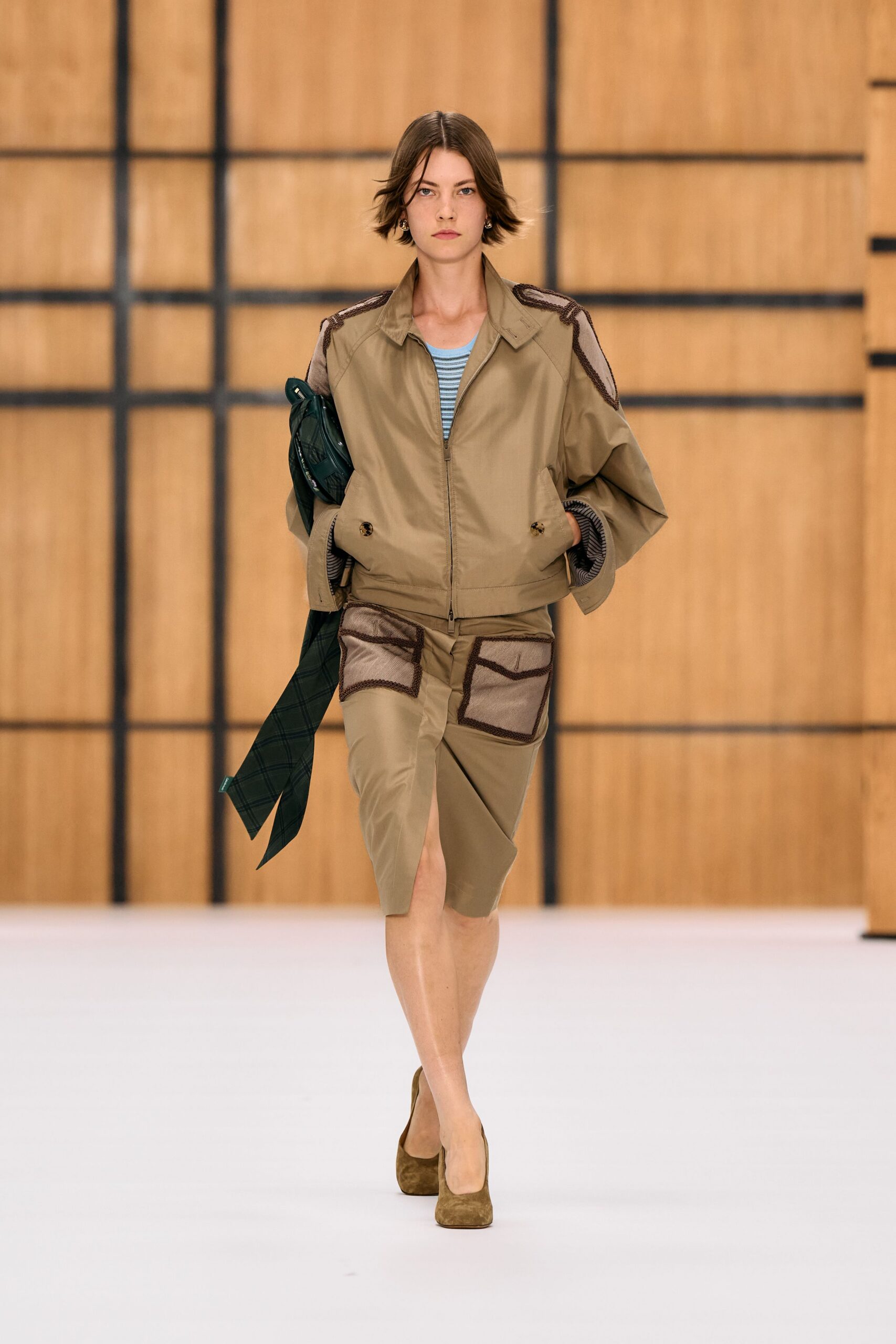 Khaki zip jacket with mesh shoulder insets outlined in dark braid. Pale blue ribbed knit peeking through the open front. Matching pencil skirt with oversized mesh patch pockets and front slit. Dark green tartan scarf tucked under one arm. Olive suede pumps. For ducking into the members bar after a long museum committee meeting.