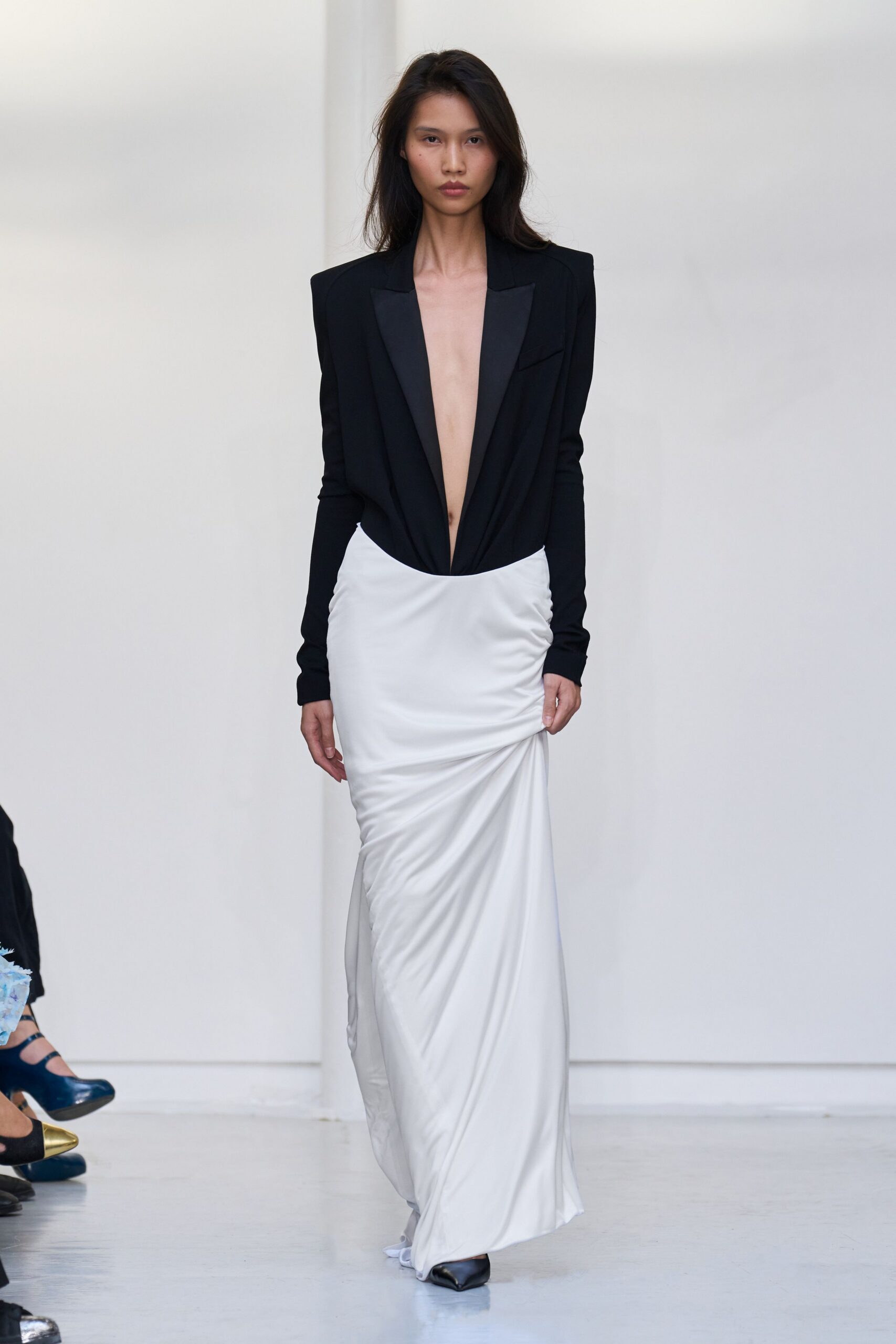 Black bodysuit cut like a tuxedo jacket, satin shawl lapels framing a plunging front. Ivory jersey column skirt, ruched at the hip and dragging slightly at the hem. Black square-toe pumps. For the courthouse elevator after the ceremony, bouquet already left behind.