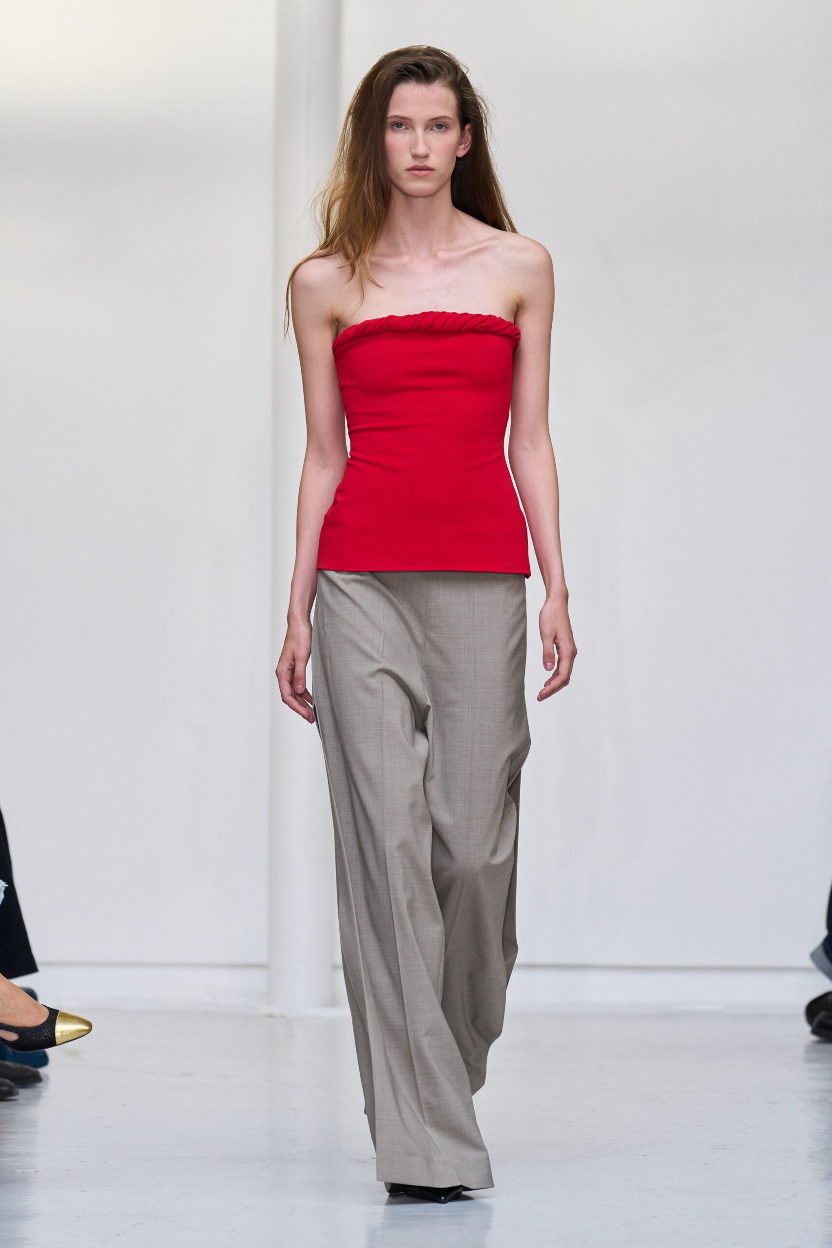 Crimson jersey tube top with a twisted rope edge at the bust. Greige wool trousers cut wide and long, breaking softly over the shoe. For crossing a plaza at noon with nowhere urgent to be.