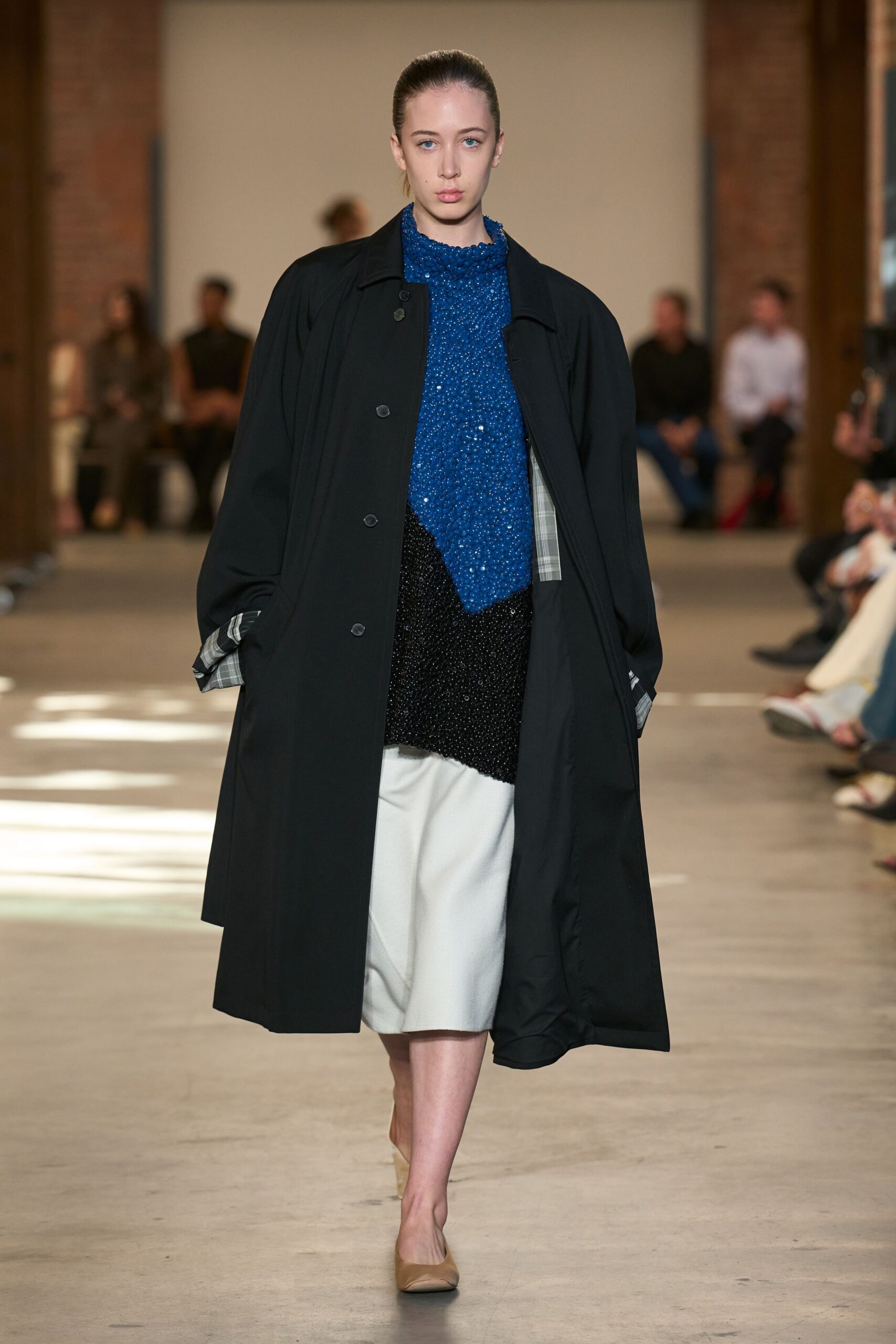 Black swing coat with grey plaid facing turned out at the cuffs. Cobalt beaded tunic, scalloped high neck and an uneven black sequin dip. White culottes in dense cloth, softly rounded through the knee. Taupe leather pumps, square at the toe. Crossing a museum atrium before the rain starts again.