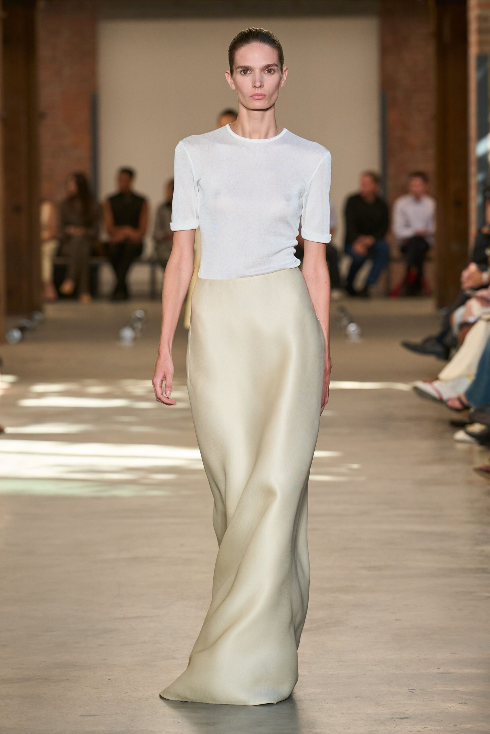 White fine-gauge knit tee, sleeves finished with narrow turned cuffs. Floor-length bias skirt in pale cream satin, pooling into a soft twist. Sunday museum atrium, footsteps echoing before the doors open.