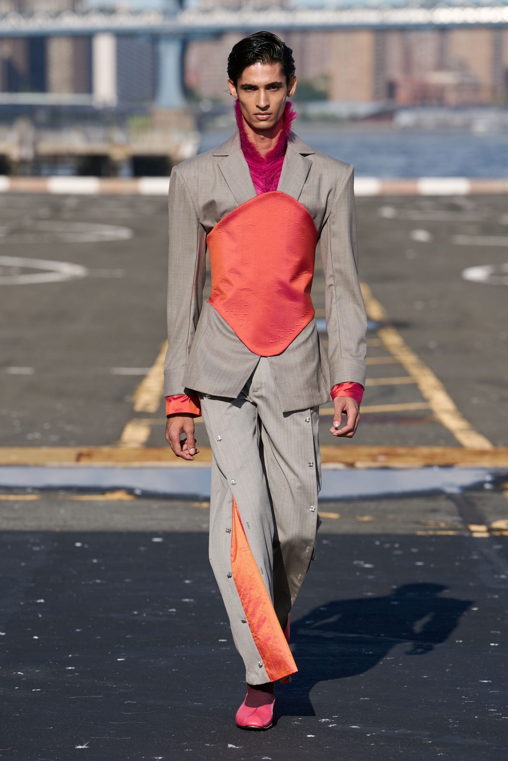 Fuchsia long-pile furry top climbing the neck like a stole. Pale greige blazer split by a coral satin shield panel. Matching straight trousers, side seams studded and opened to coral insets. Dark plum ribbed socks. Bubblegum leather flats with a center seam. Crossing the ferry lot after sunrise with river wind still in it.